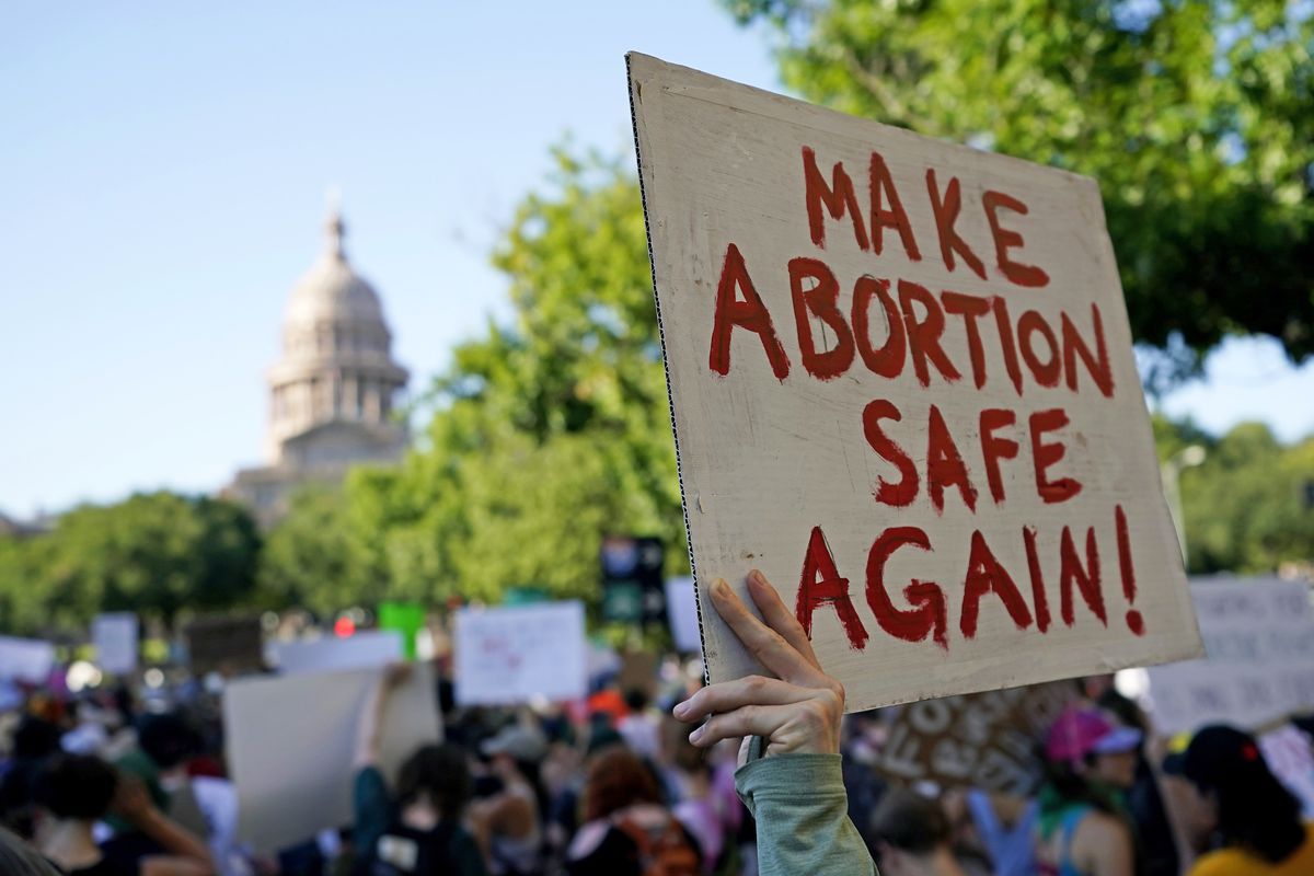 A protester holds up a sign that reads, “Make abortion safe again!” The Austin statehouse is in the background.