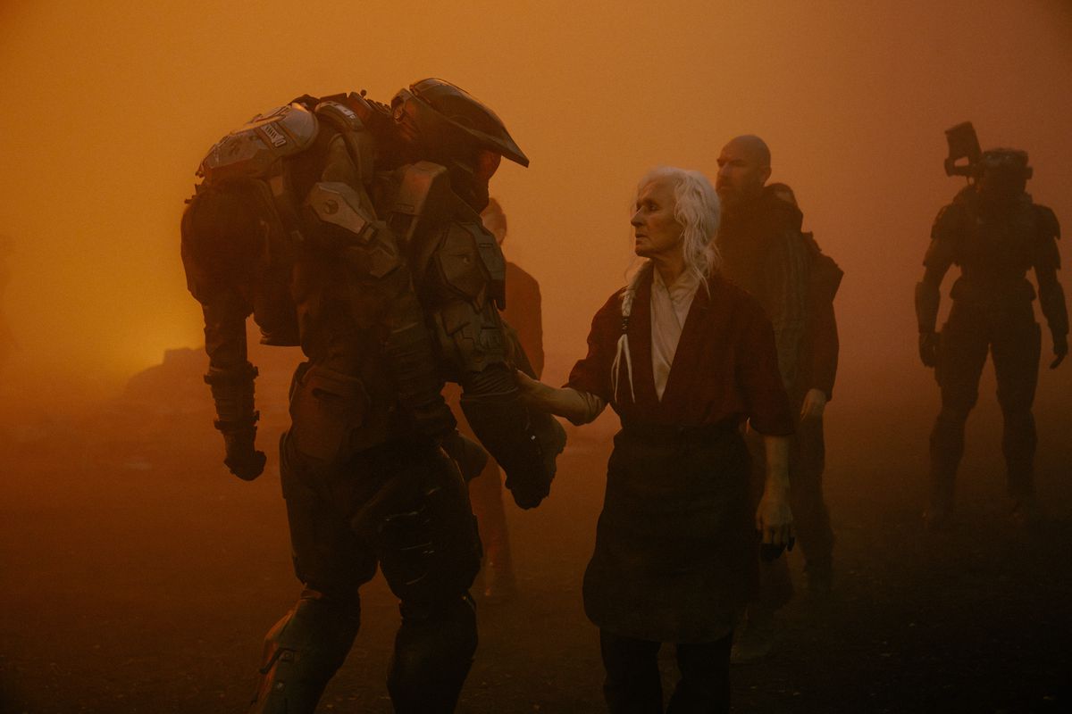 مستر چیف یک تفنگدار دریایی مجروح را روی شانه خود حمل می کند که آتش و خاکستر آسمان را در فصل دوم Halo می پوشاند.