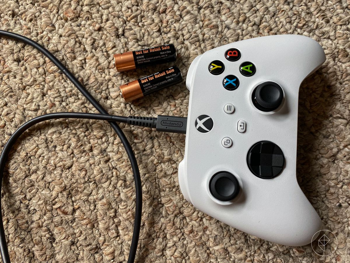 an overhead shot of the Xbox Series S controller sitting on beige carpet next to a pair of AA batteries, with a Nintendo-branded USB-C cable plugged into it