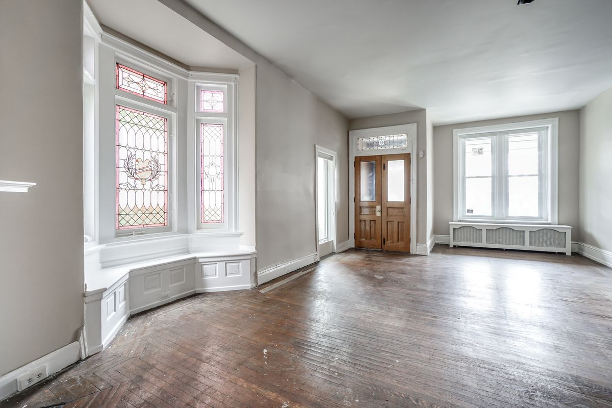 A spacious living room with hardwood floors, a bay window with stained glass windows. 
