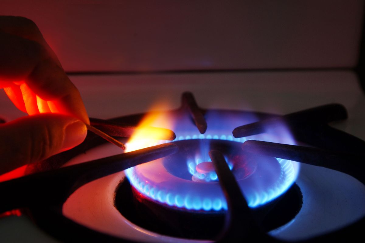 A person holds a match in the flame of a gas stove burner.