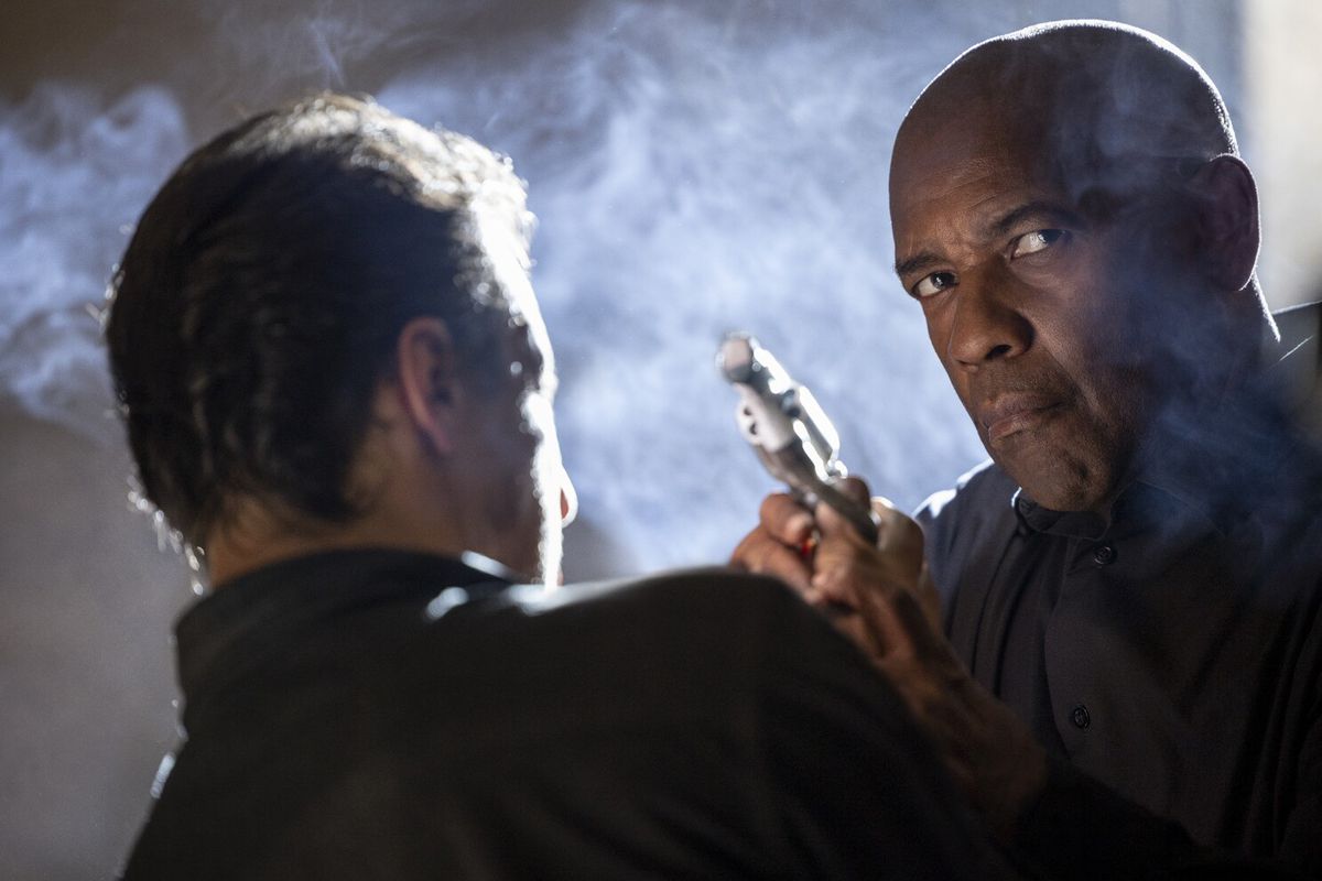 Denzel Washington as Robert McCall aiming a pistol over the shoulder of a man in The Equalizer 3.
