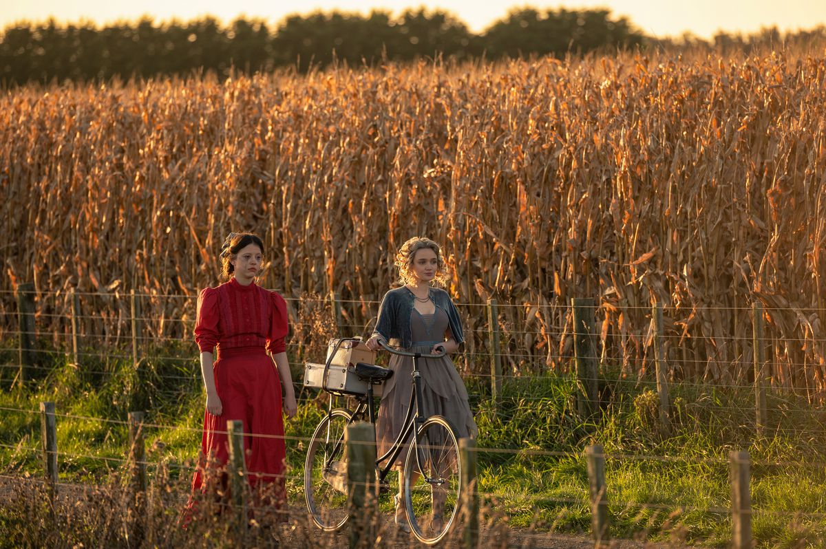 Pearl (Mia Goth) in Ti West's Pearl walks alongside her sister-in-law Misty (Emma Jenkins-Purro) at the edge of a vast dead cornfield in Pearl