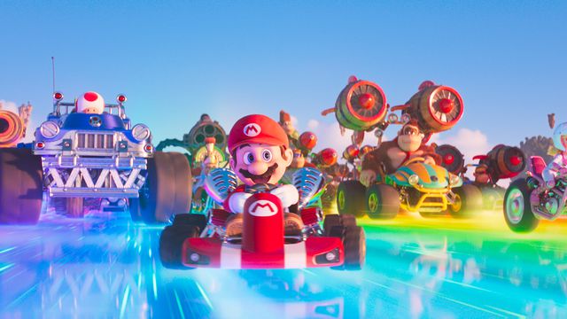 Mario and the cast of the Mario Bros. Movie in their Mario Kart vehicles as they speed down Rainbow Road.