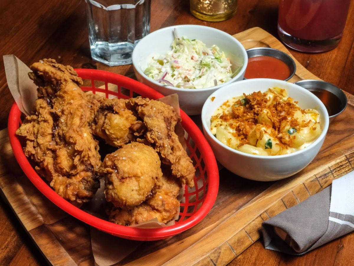 A basket of fried chicken next to a bowl of mac ‘n’ cheese and a bowl of cole slaw.