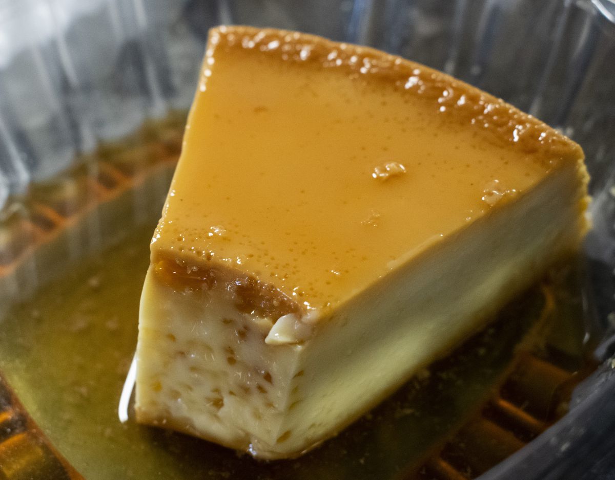 A triangular slice of flan with a bite taken out in a plastic clamshell container