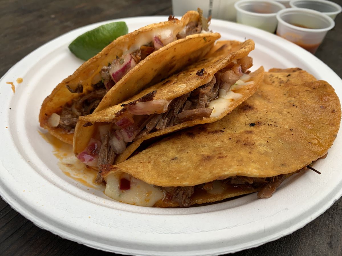 Three birria tacos on a paper plate, with a wedge of lime