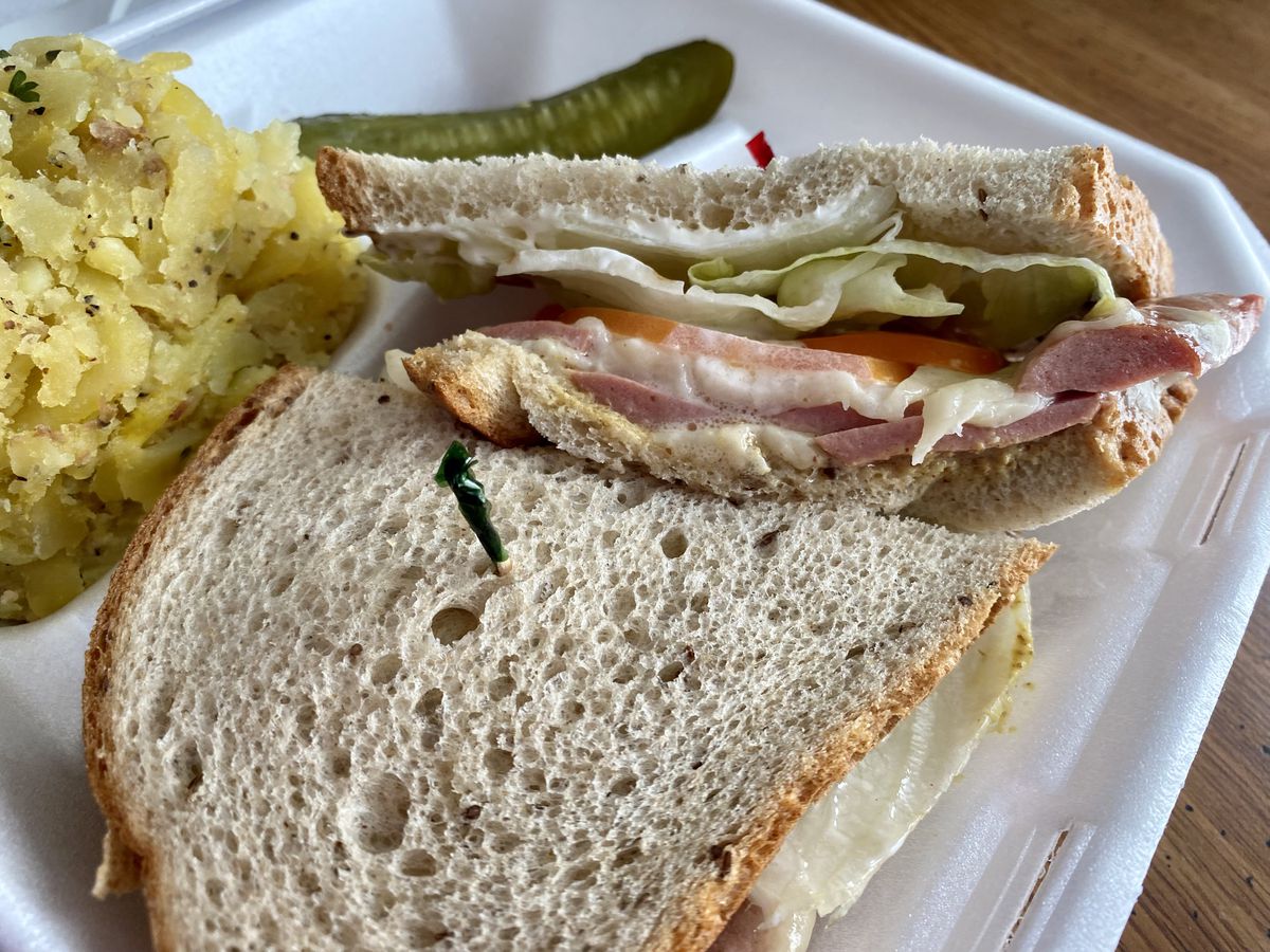 A sandwich with pickles and potatoes in a takeout container.