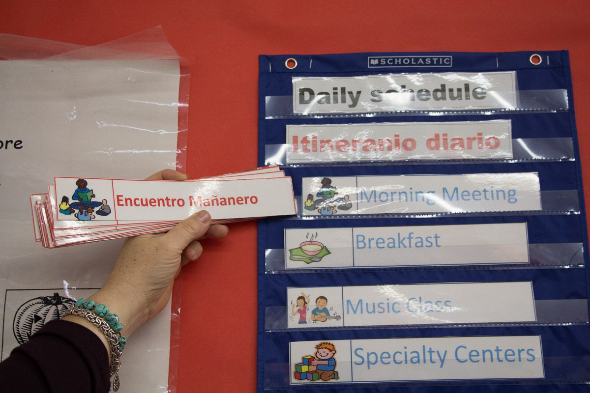 A teacher points to her class' daily schedule, with laminated cards written in both English and Spanish.