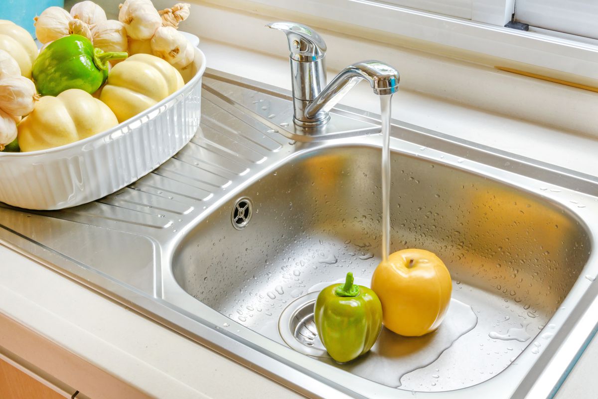 Two fruits in a sink being washed in water from a faucet.