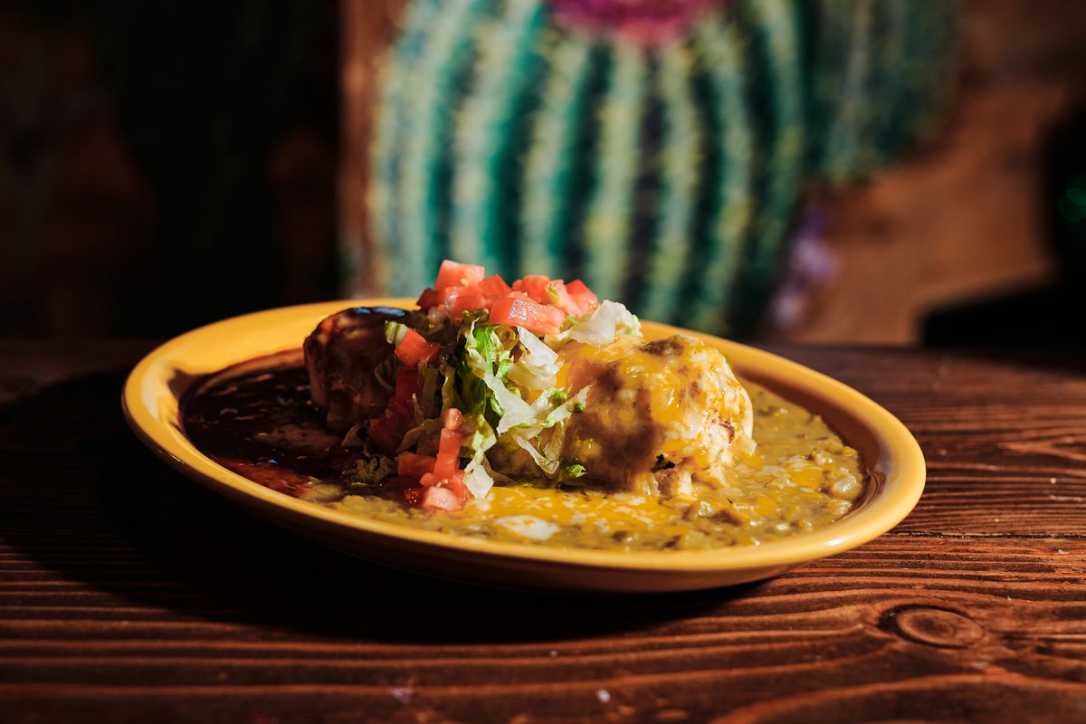 A Christmas-style burrito with smothered sauces is served on a yellow plate on a wooden table.