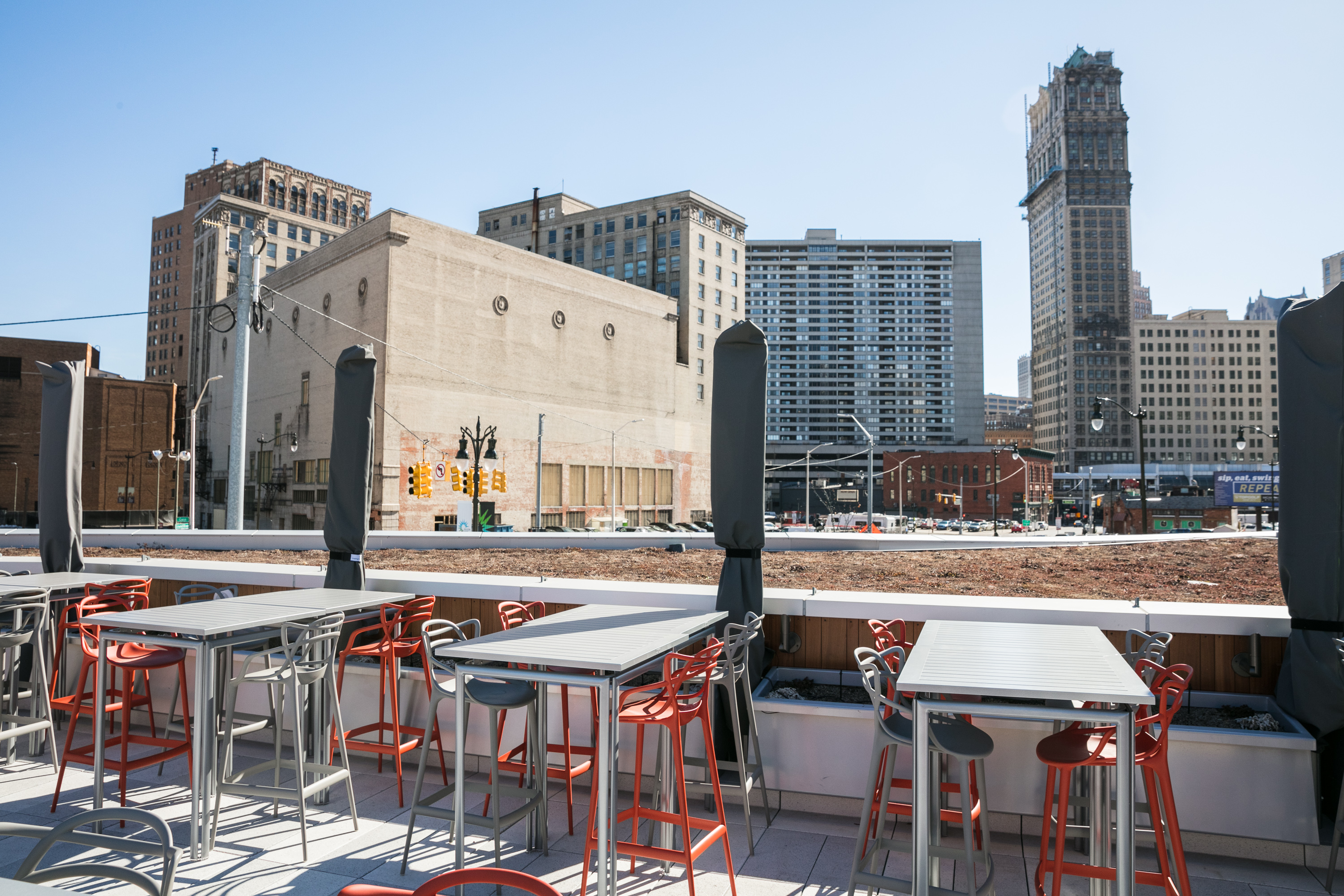 Rooftop building with tables and chairs shows views of downtown Detroit buildings