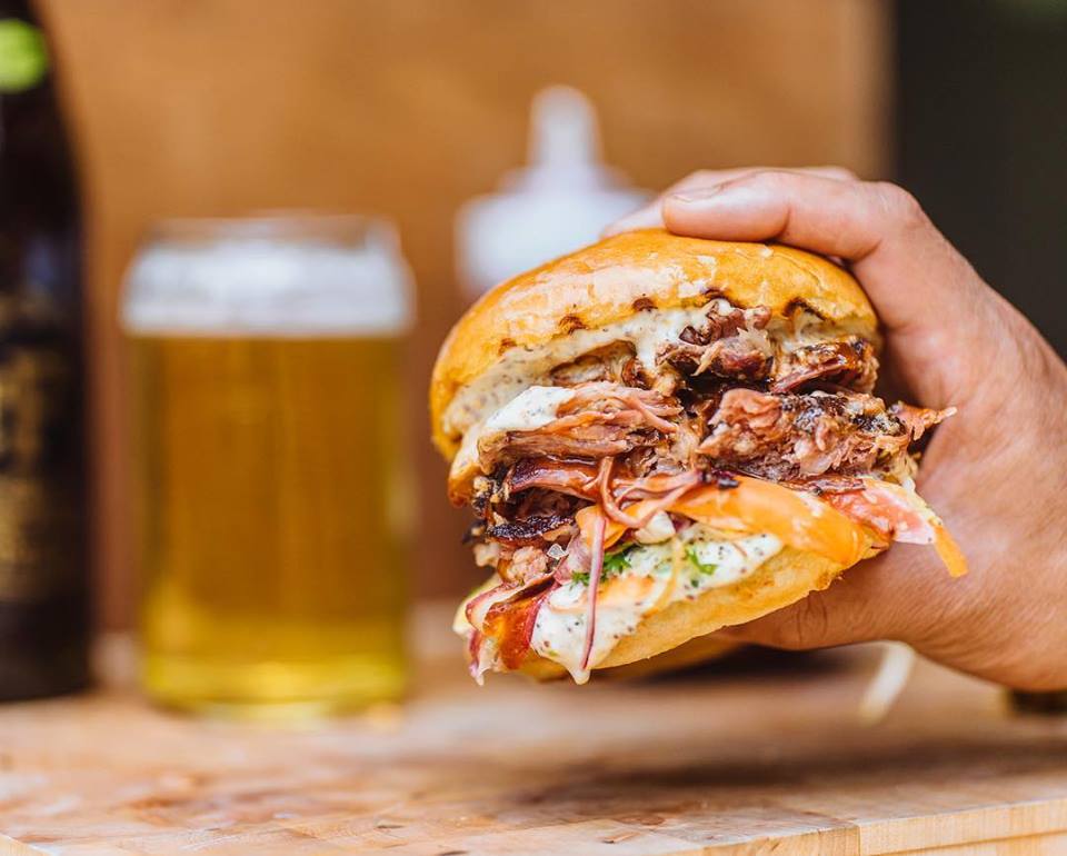 A hand holds a pulled pork sandwich