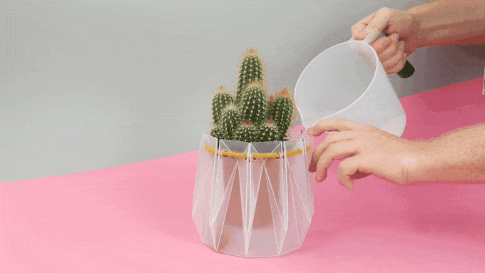 An animated image of a person pouring water into the folded plastic planter holding a potted cactus inside. 