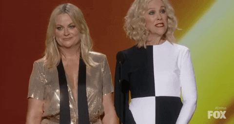 amy poehler in a gold dress standing on the emmys stage next to catherine o hara saying “pokemon”