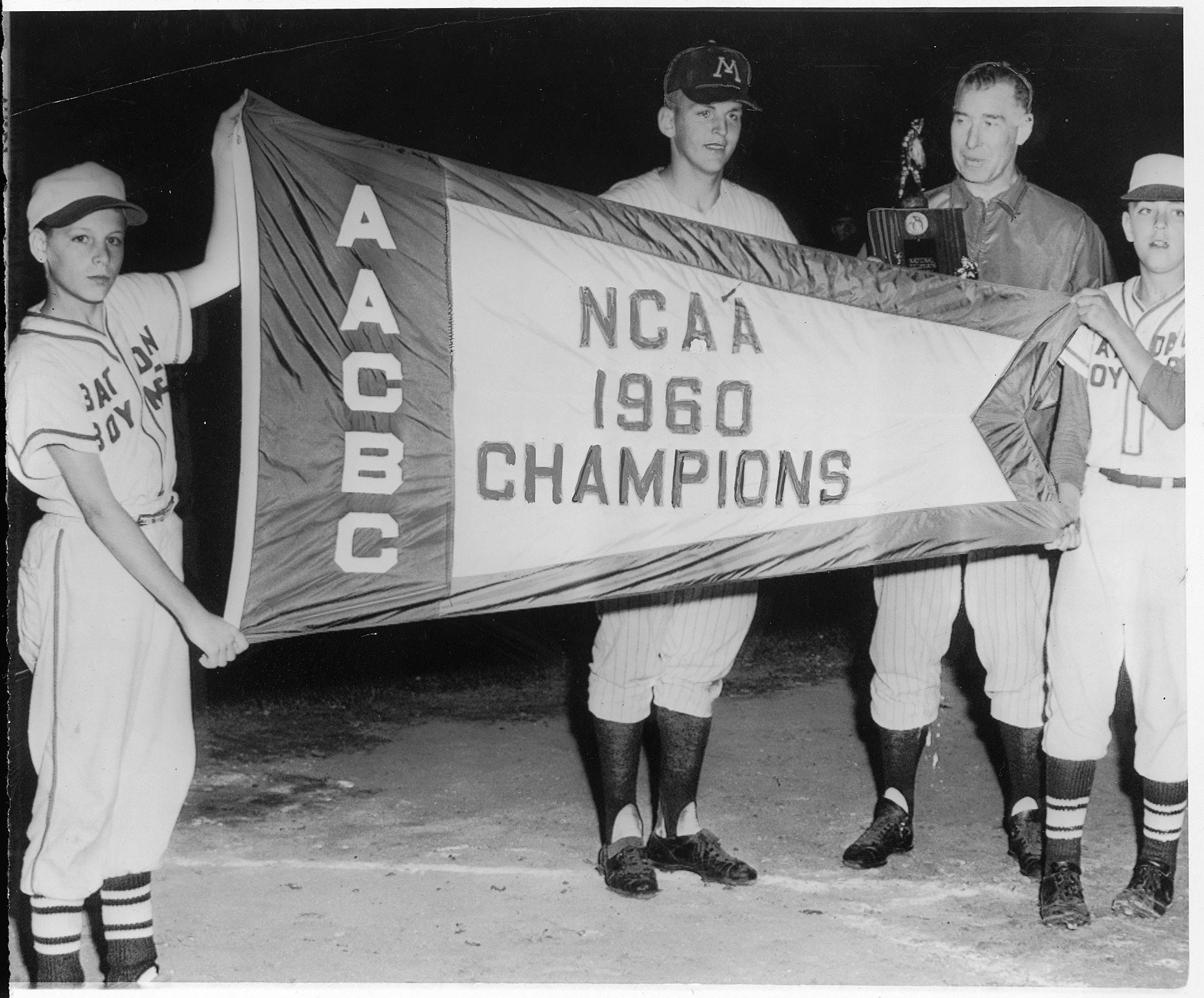 Batboys Don Noel and Dave Benson held up a 1960 NCAA championship flag for Gophers team MVP John Erickson and coach Dick Siebert.