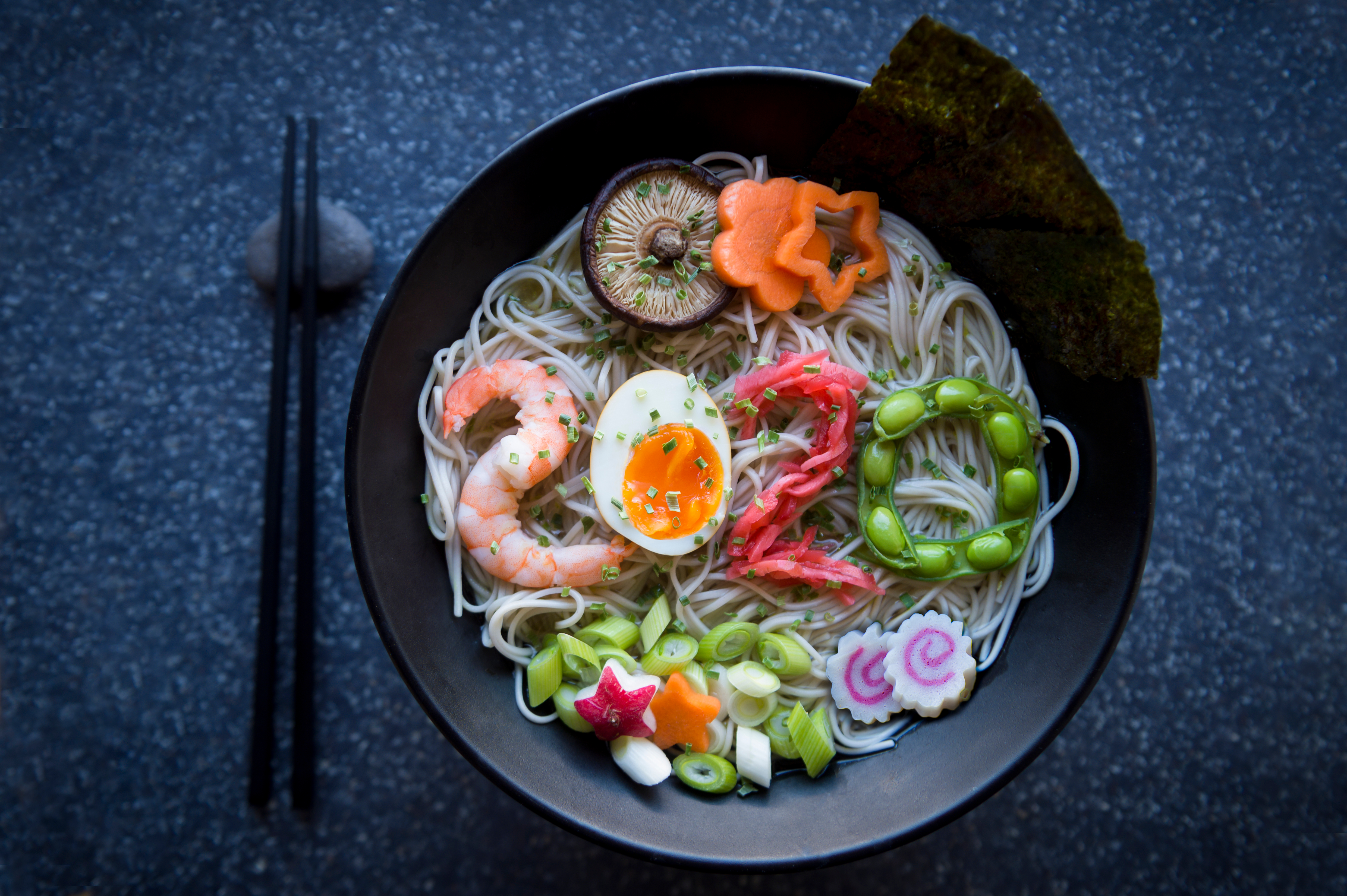 Bowl of Japanese buckwheat ramen noodle soup topped with the number 2020 spelled out of shrimp, boiled egg, pickled ginger, and edamame beans