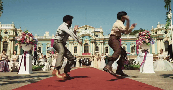 Bheem and Ram dance down a red carpet in front of an English palace