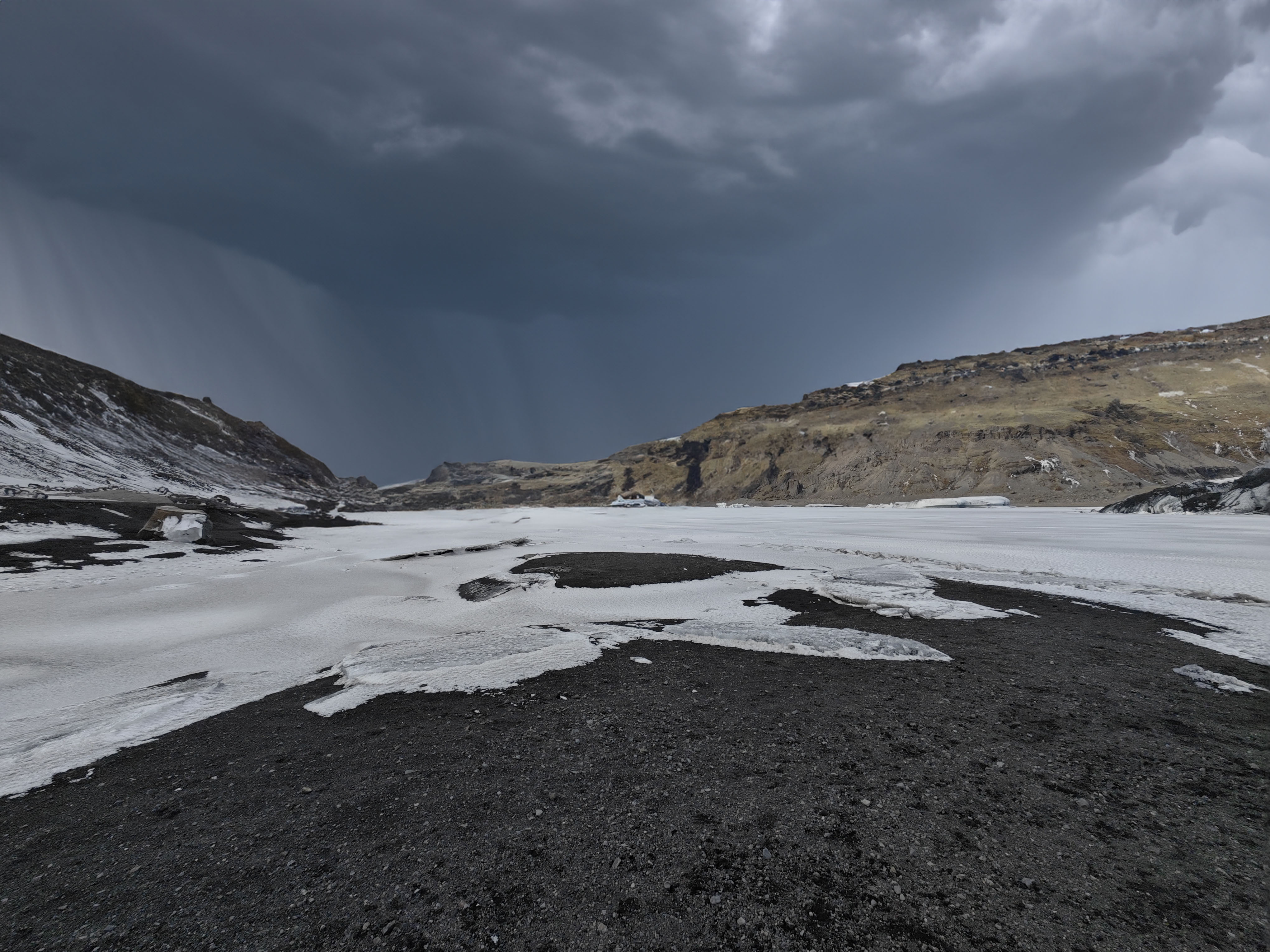 Photo of valley with snow and a dark rain cloud above.