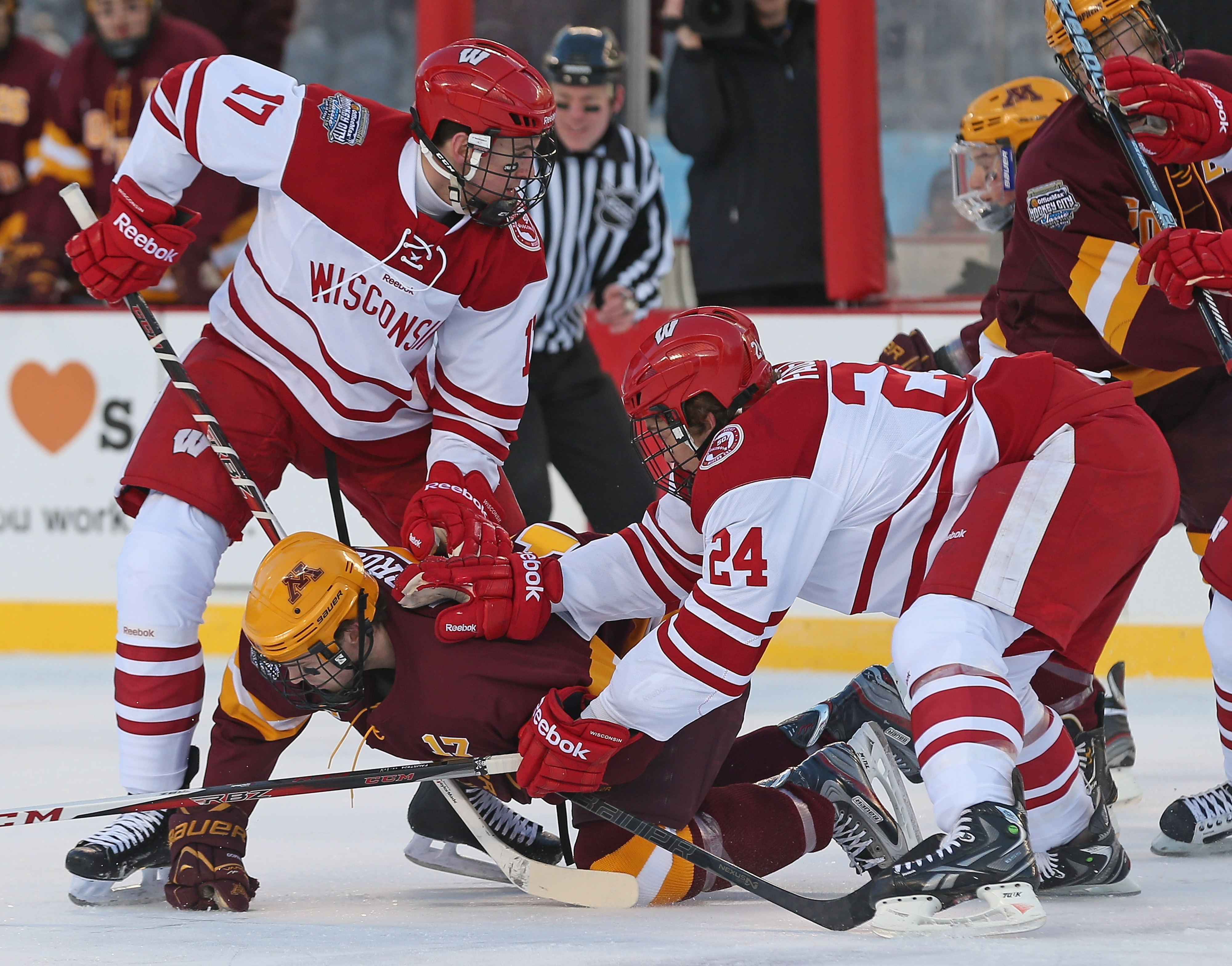 Seth Ambroz #17 of the Minneosta Golden Gophers is shoved to the ice by Joe Faust #24 and Nic Kerdiles #17 of the Wisconsin Badgers during the Hockey City Classic at Soldier Field on February 17, 2013 in Chicago, Illinois.