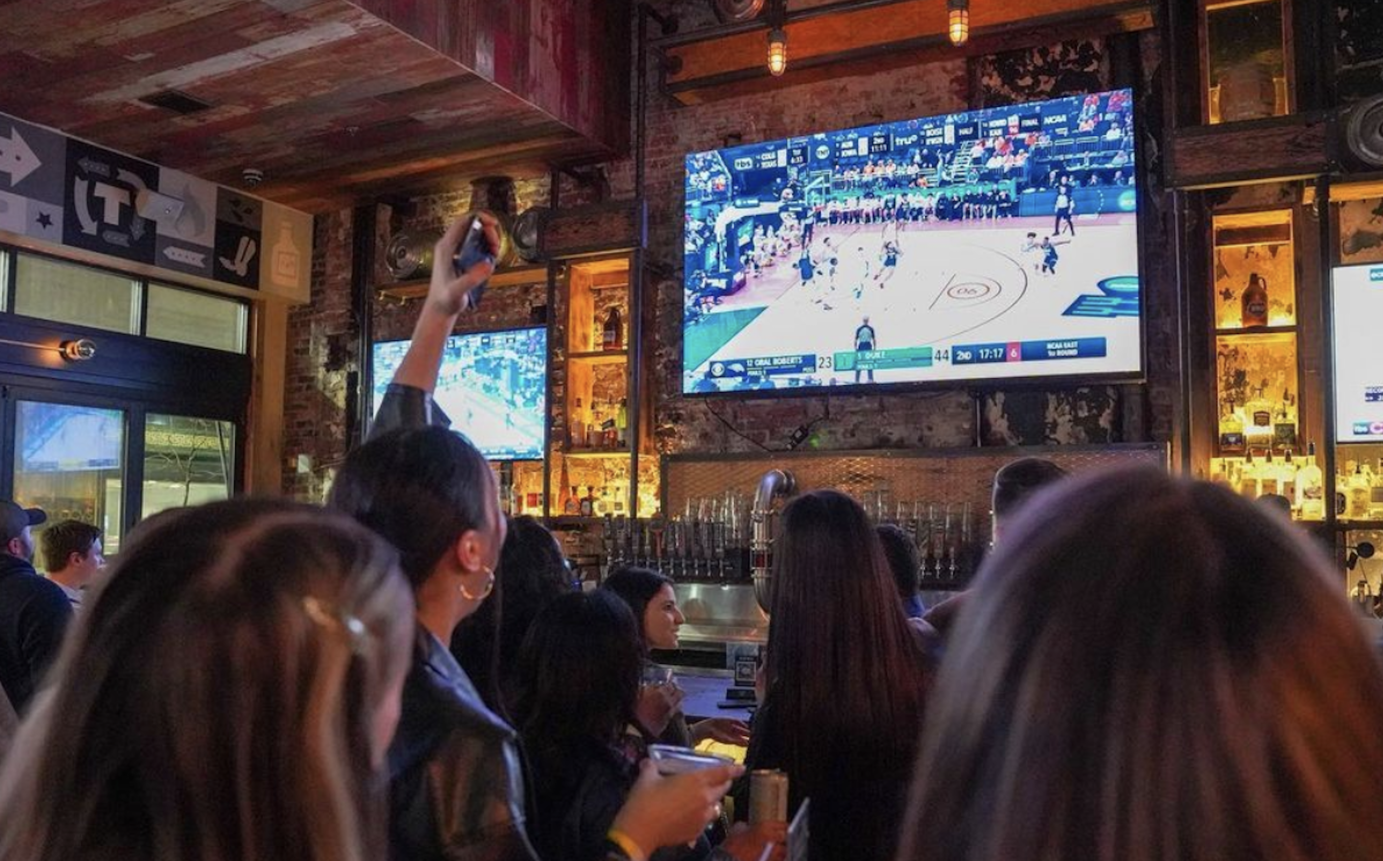 A group of people at a bar watching sports game on a big screen TV. 
