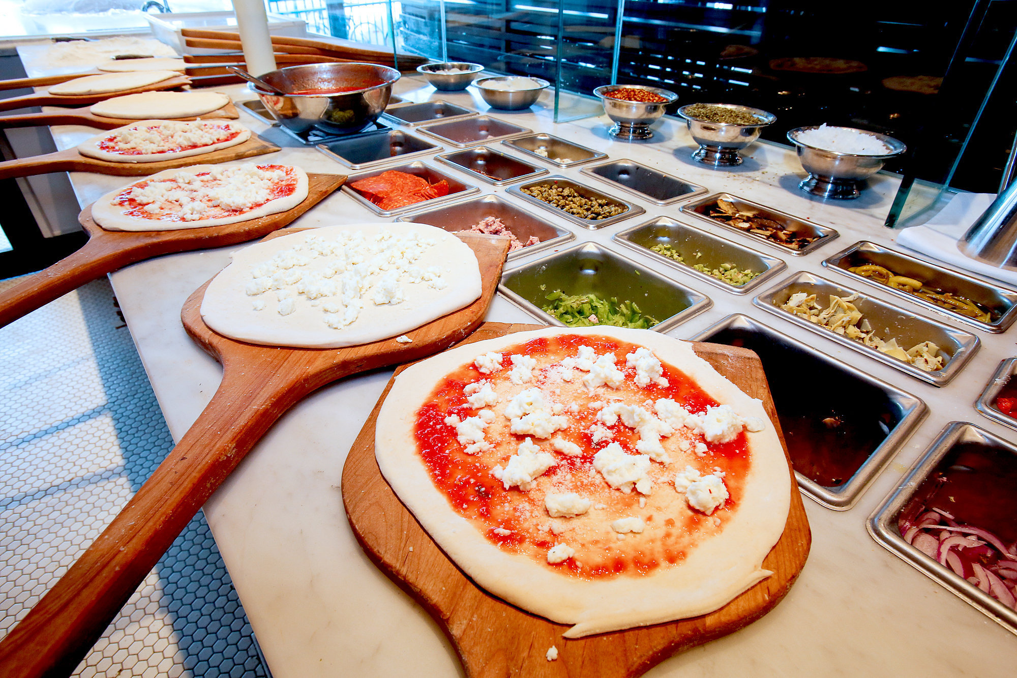 Pizzas lined up on a counter for topping