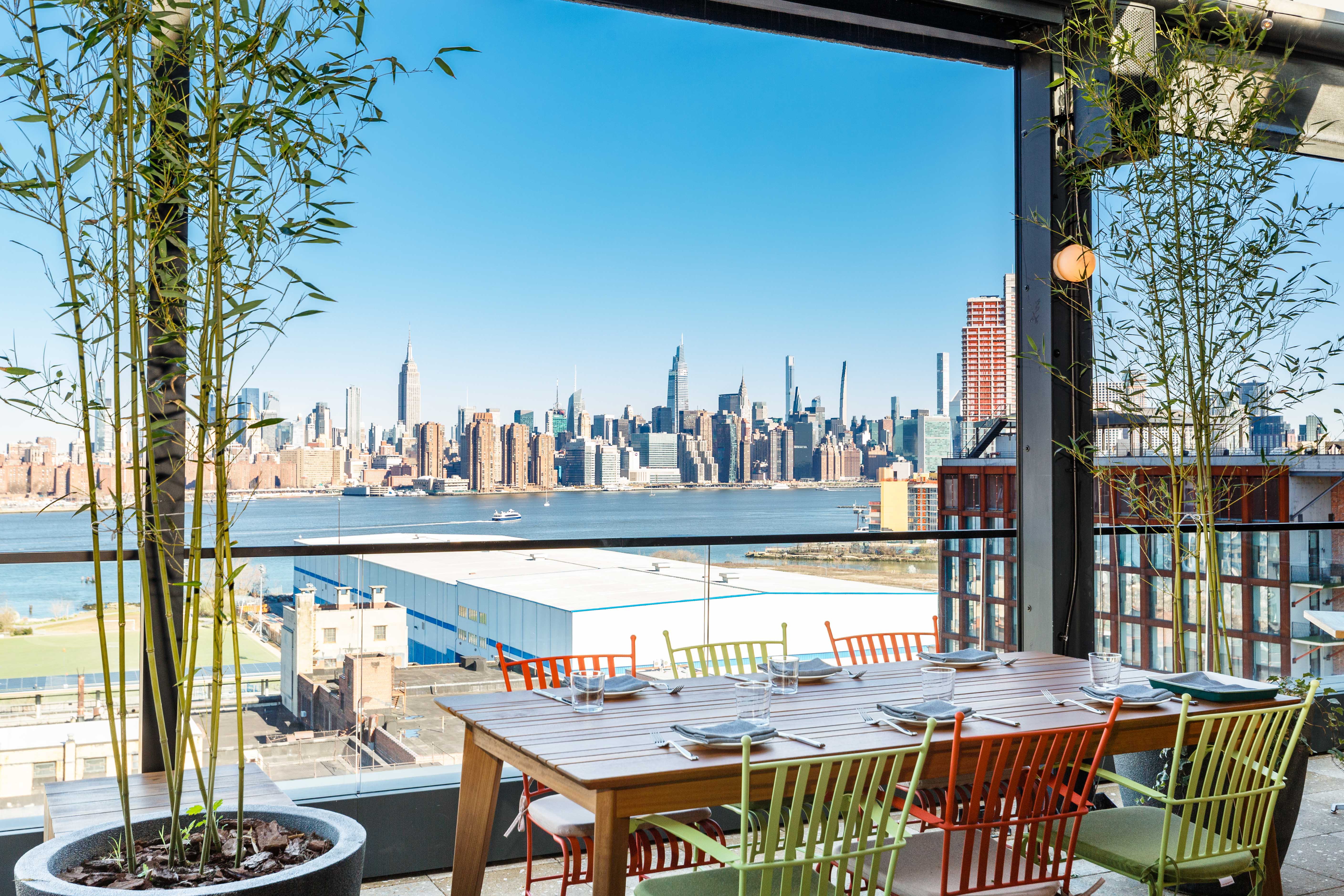 A table with multi-colored chairs in the foreground, set against a backdrop of the Manhattan skyline.