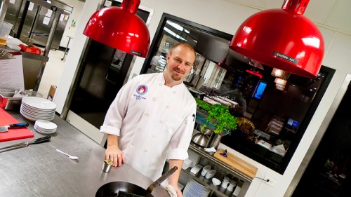 Executive chef (and not a student), Kris Jakob standing in front of a hydroponic herb garden in the kitchen.