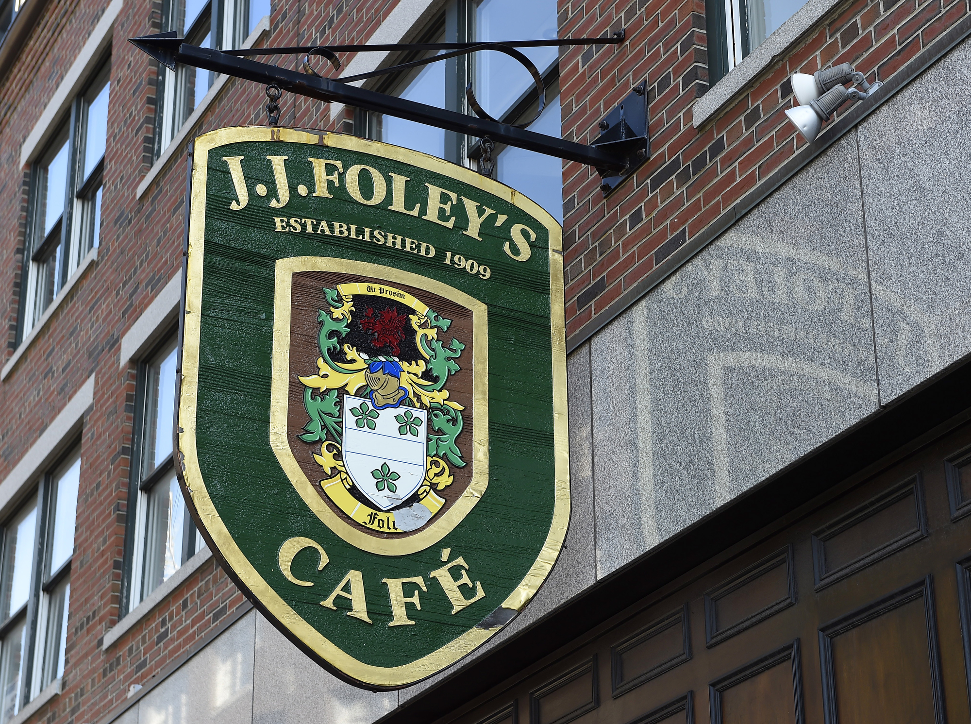 A green and gold restaurant sign hanging off the side of a building with a coat of arms pictured and “J.J. Foley’s Cafe” written on the side.