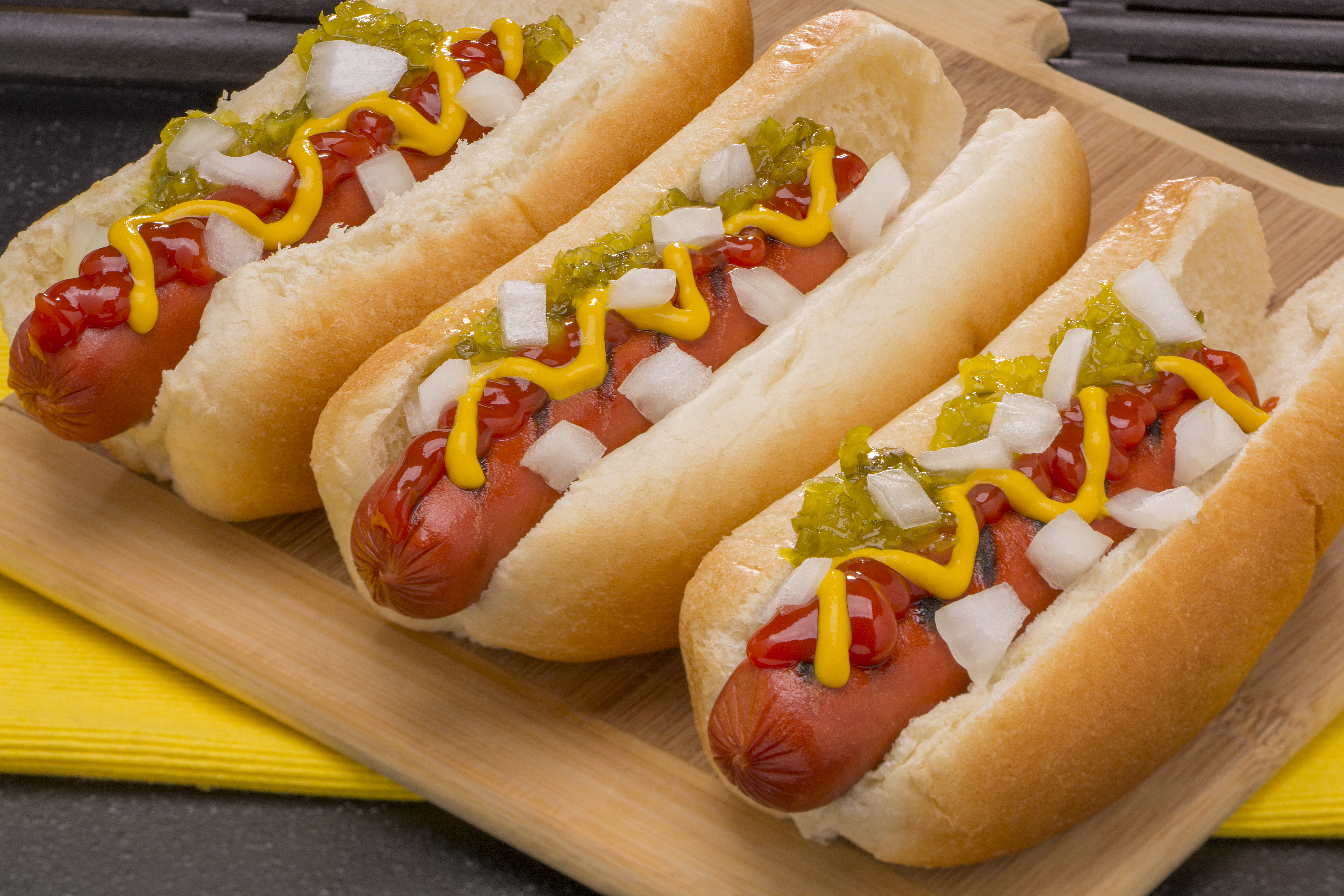 A close up image of three hot dogs topped with relish, onion and mustard