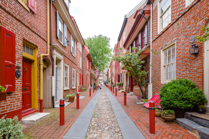 An alley in Philadelphia. On both sides of the alley are buildings with red brick facades and colorful doors.