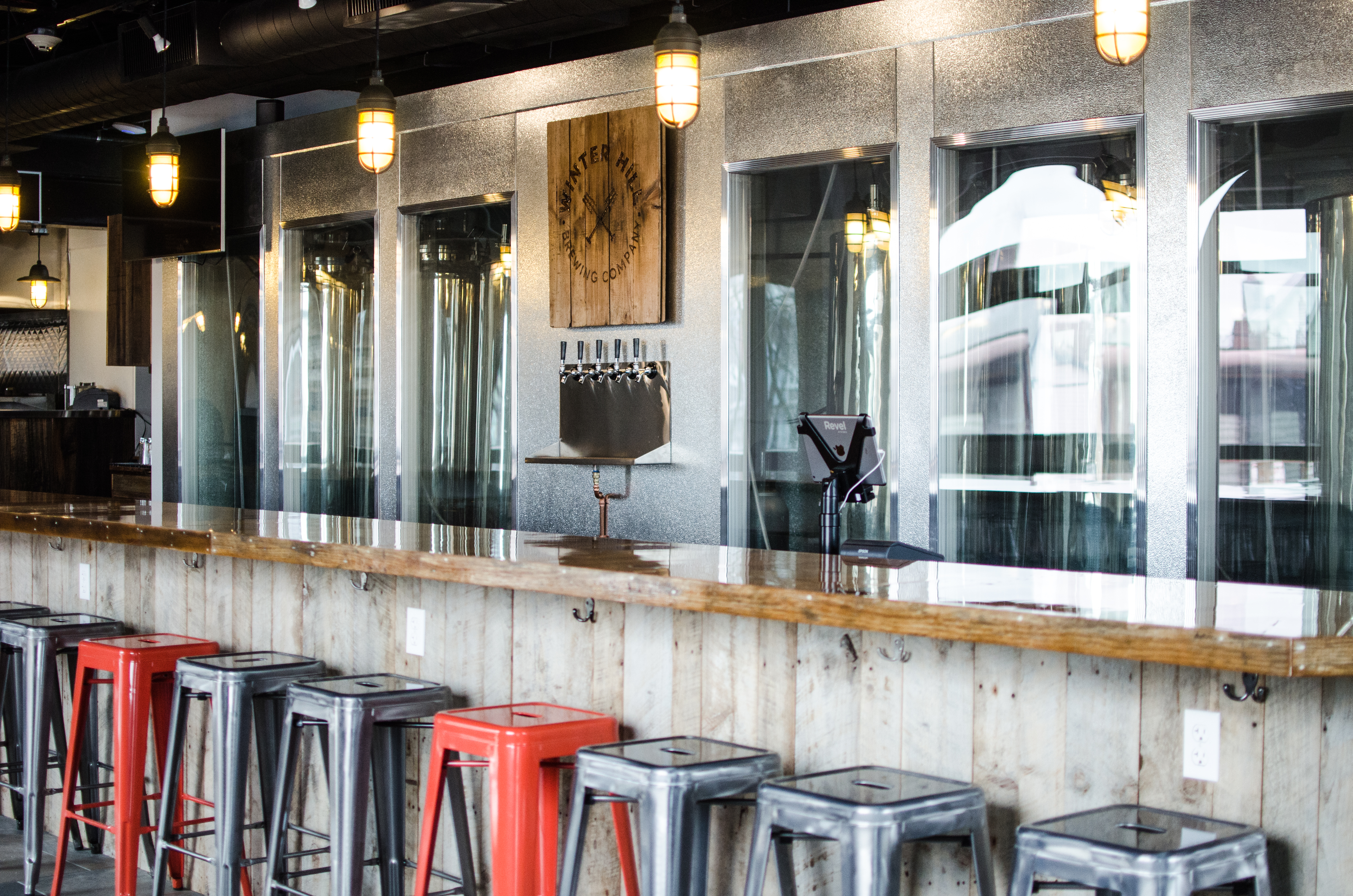 Interior shot of the bar at a brewery. A glossy wooden bar has red and silver metal stools.
