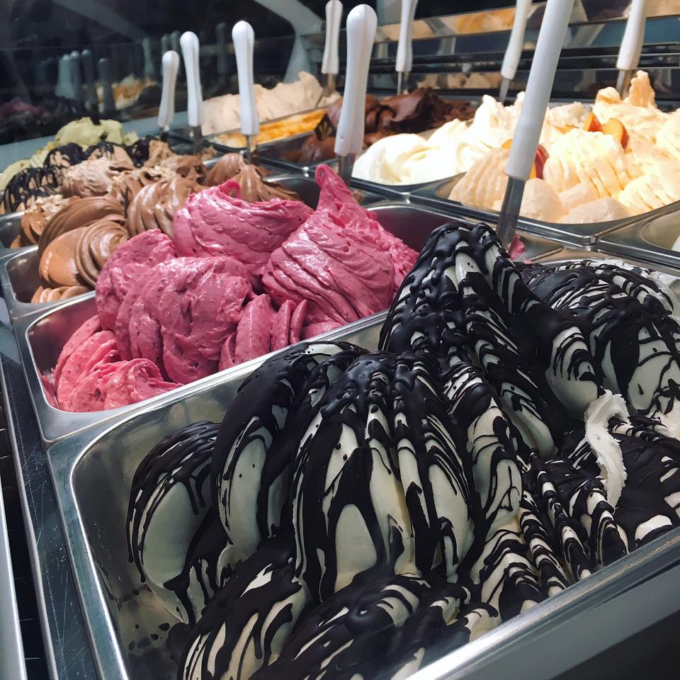 10 colorful flavors of gelato are visible in a gelato shop display, each in a metal bin with a spoon sticking out of it