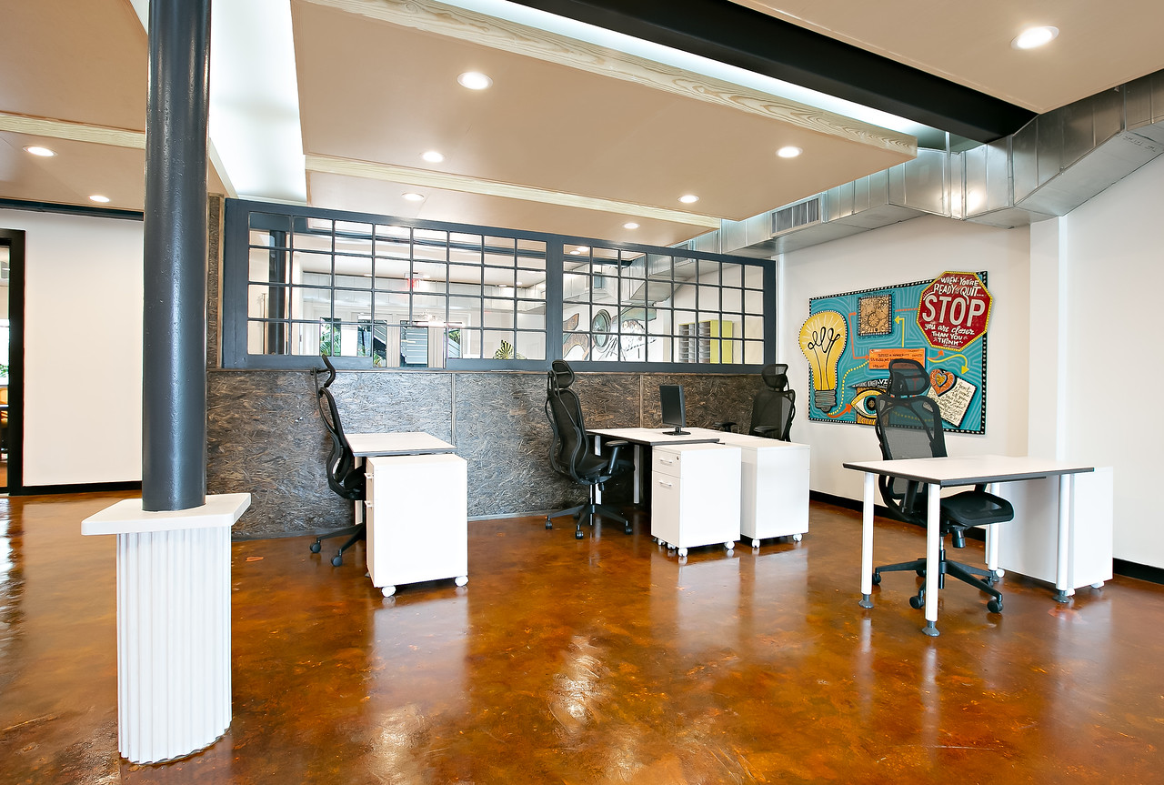 A white office with black columns and a colorful mural is filled with four desks.