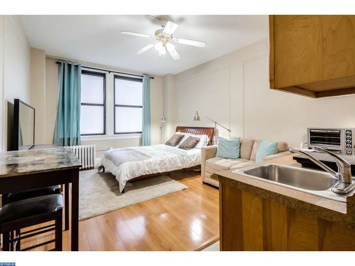 A bright but small studio with a ceiling fan, hardwood floors, and two big windows.