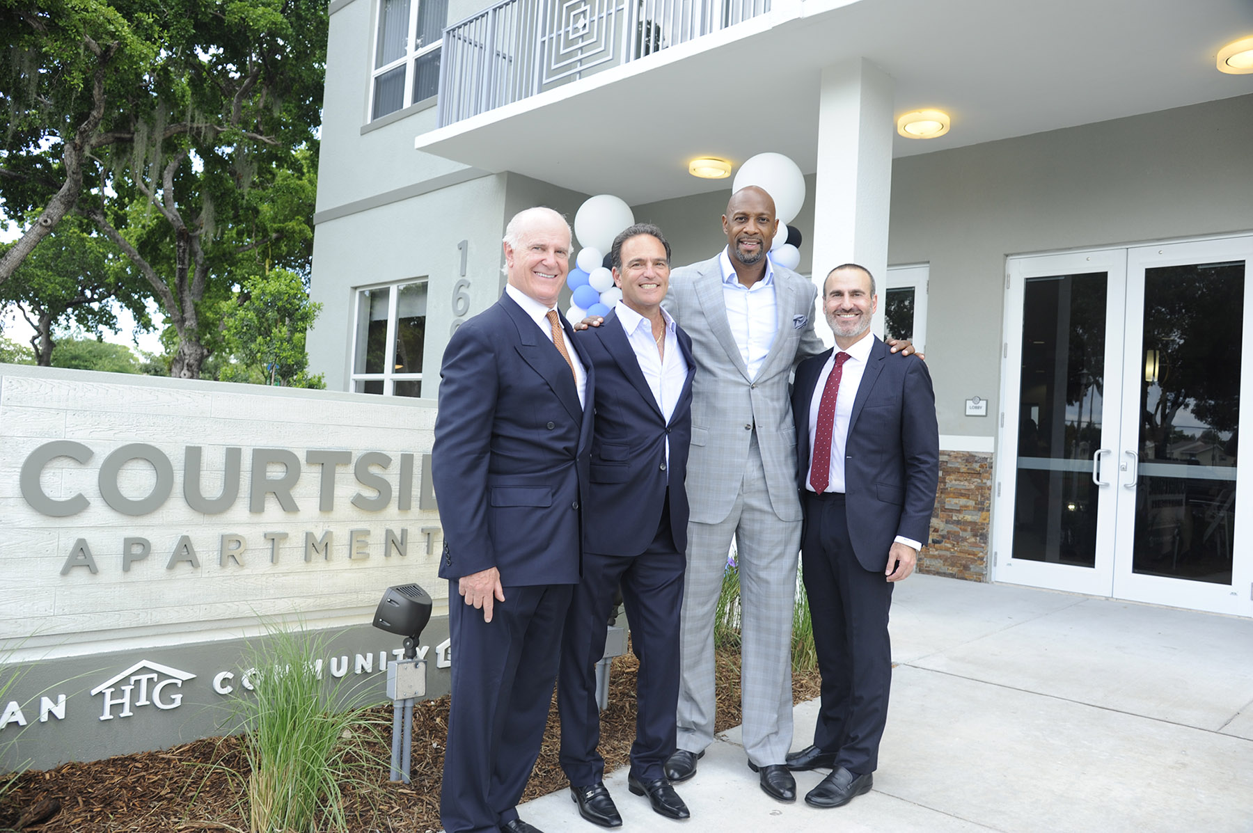 Randy Rieger, Allen Furst, Alonzo Mourning, and Matthew Rieger in front of a grey affordable housing complex in Overtown