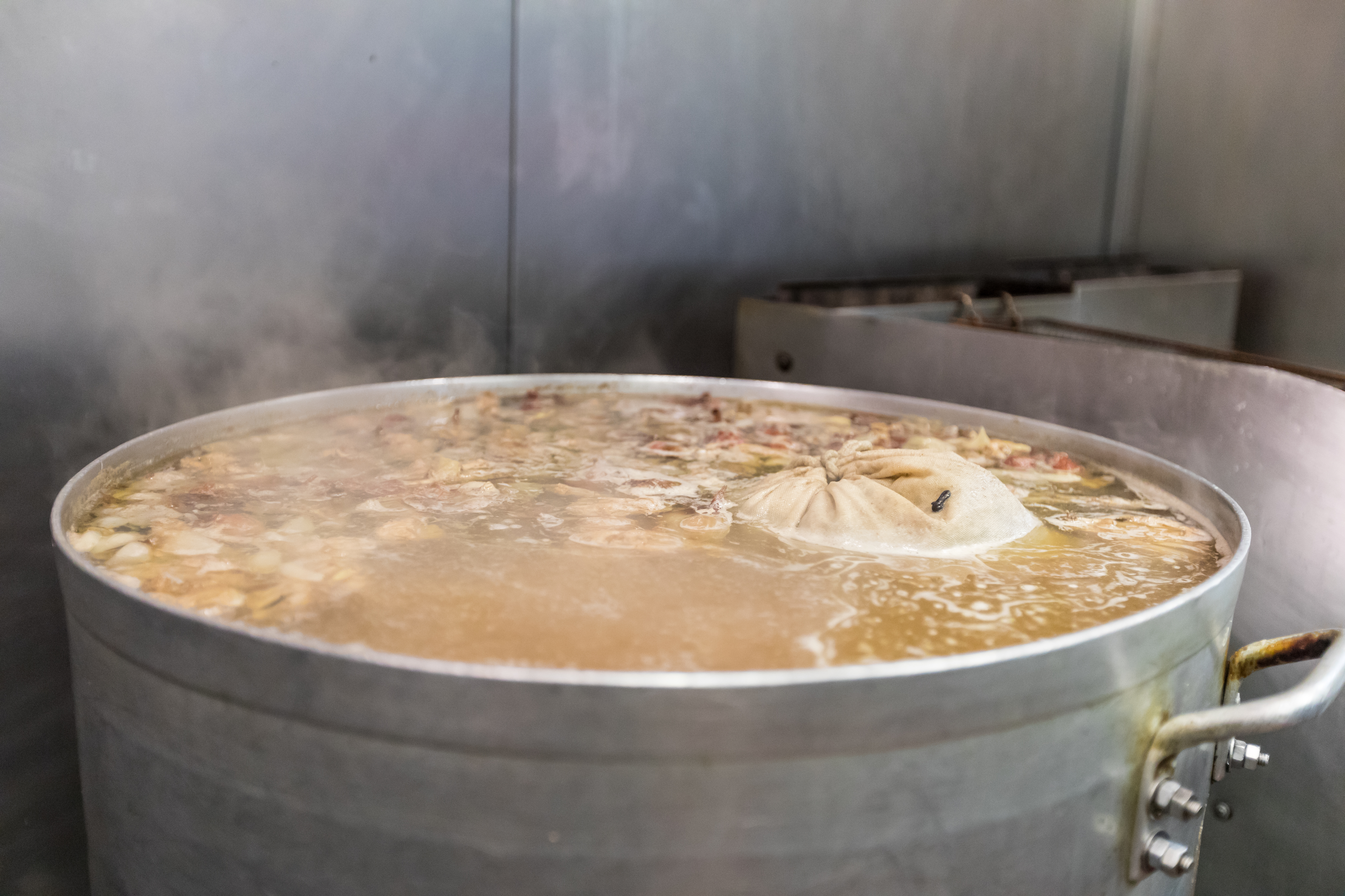 A large pot of broth with a package of spices floating on top of it as it simmers.