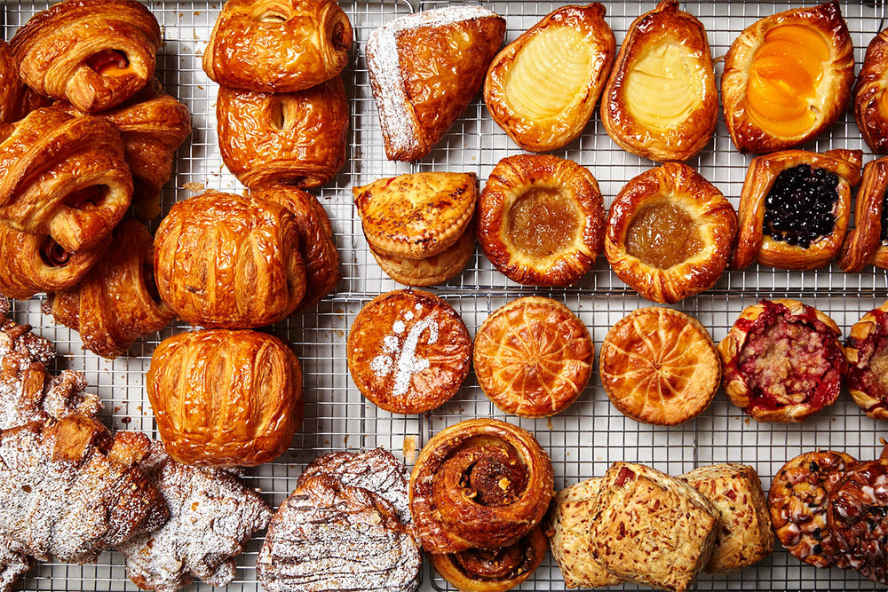 A top-down view of croissants, tarts, and other pastries on a baking sheet.
