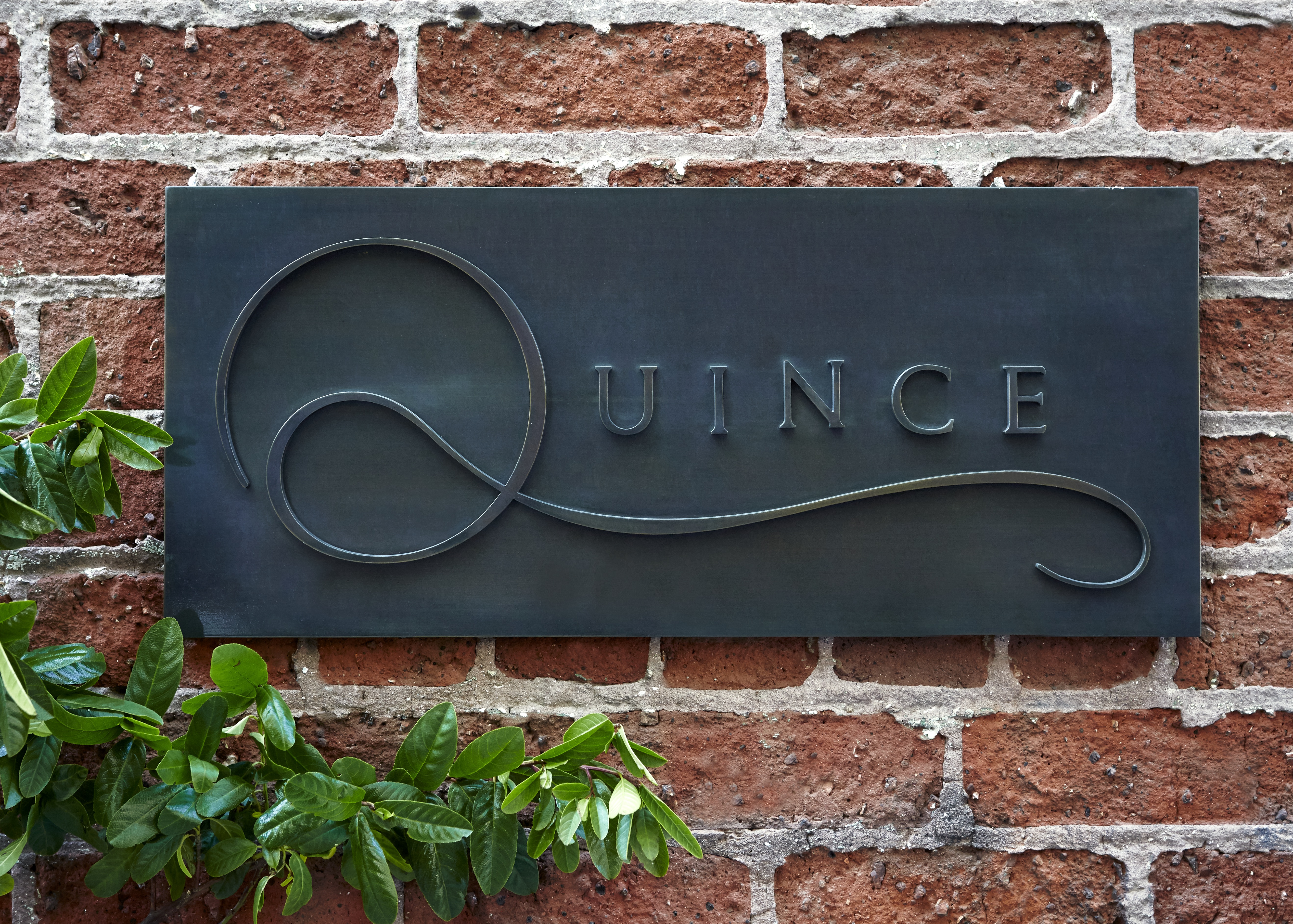 A sign on a brick wall that says “Quince.”