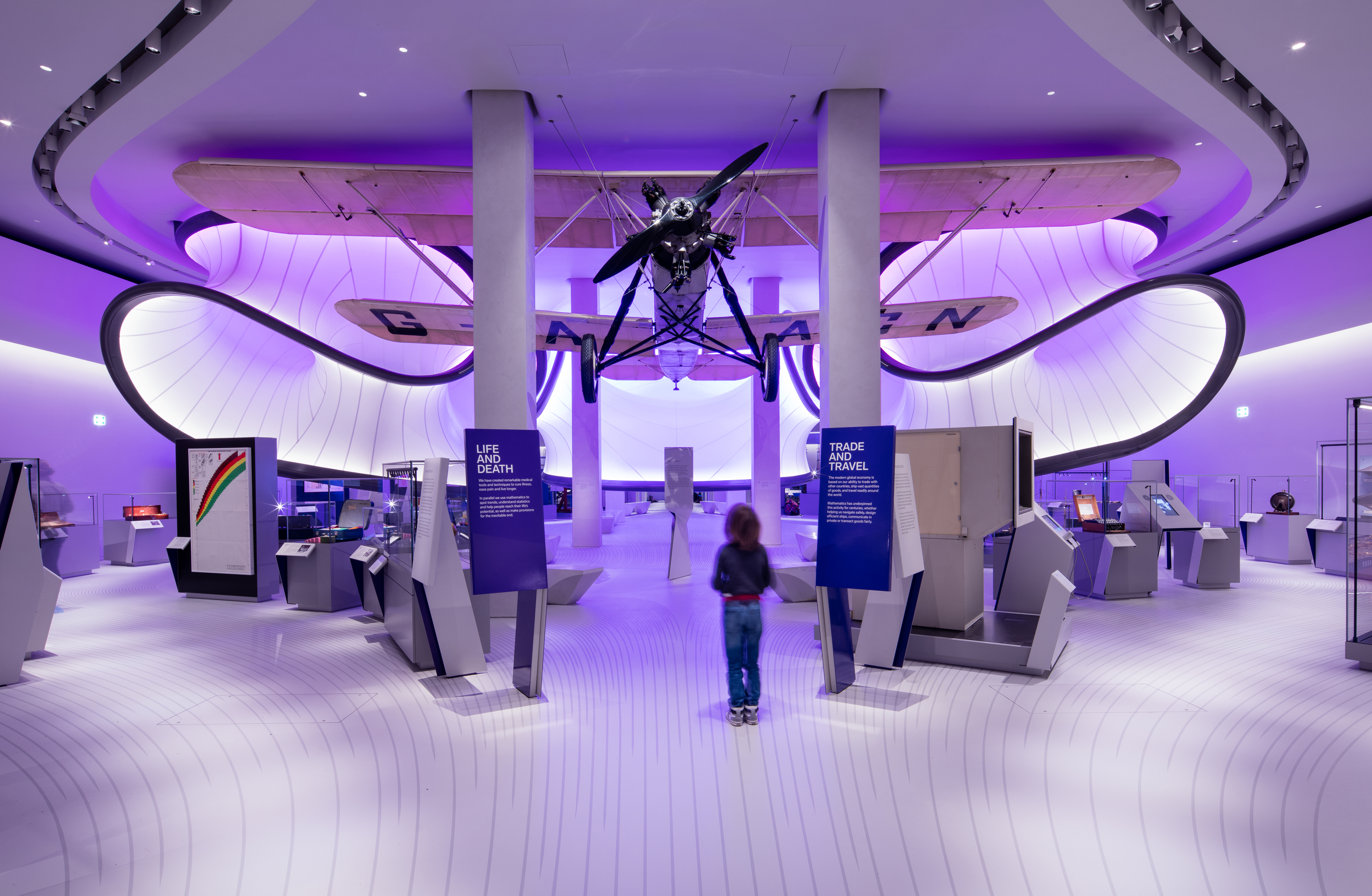 Interior shot of gallery with hanging aircraft and large curving ribbons floating above exhibition space. 
