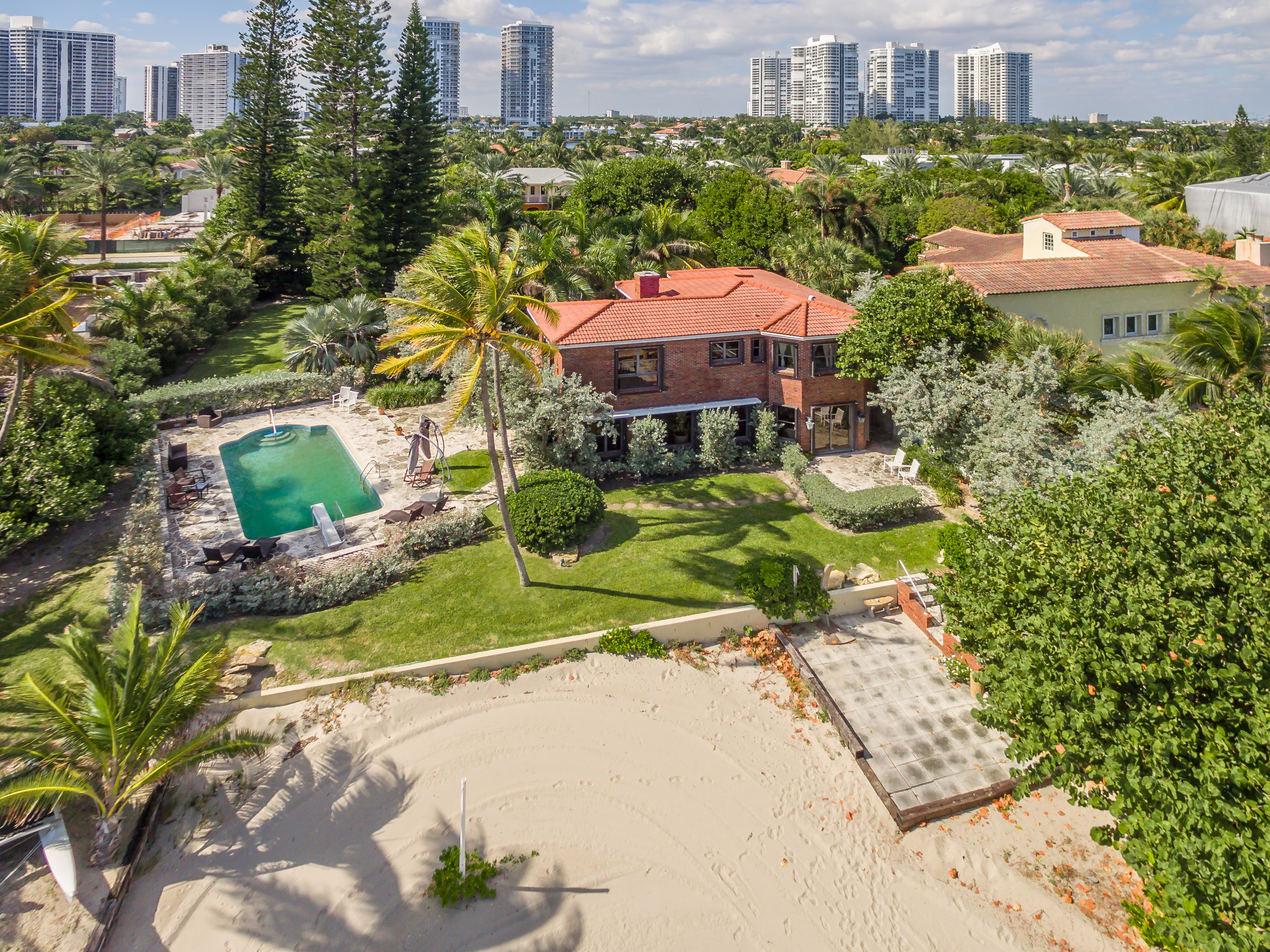Aerial of a beachfront home with a red roof, private beach and a pool