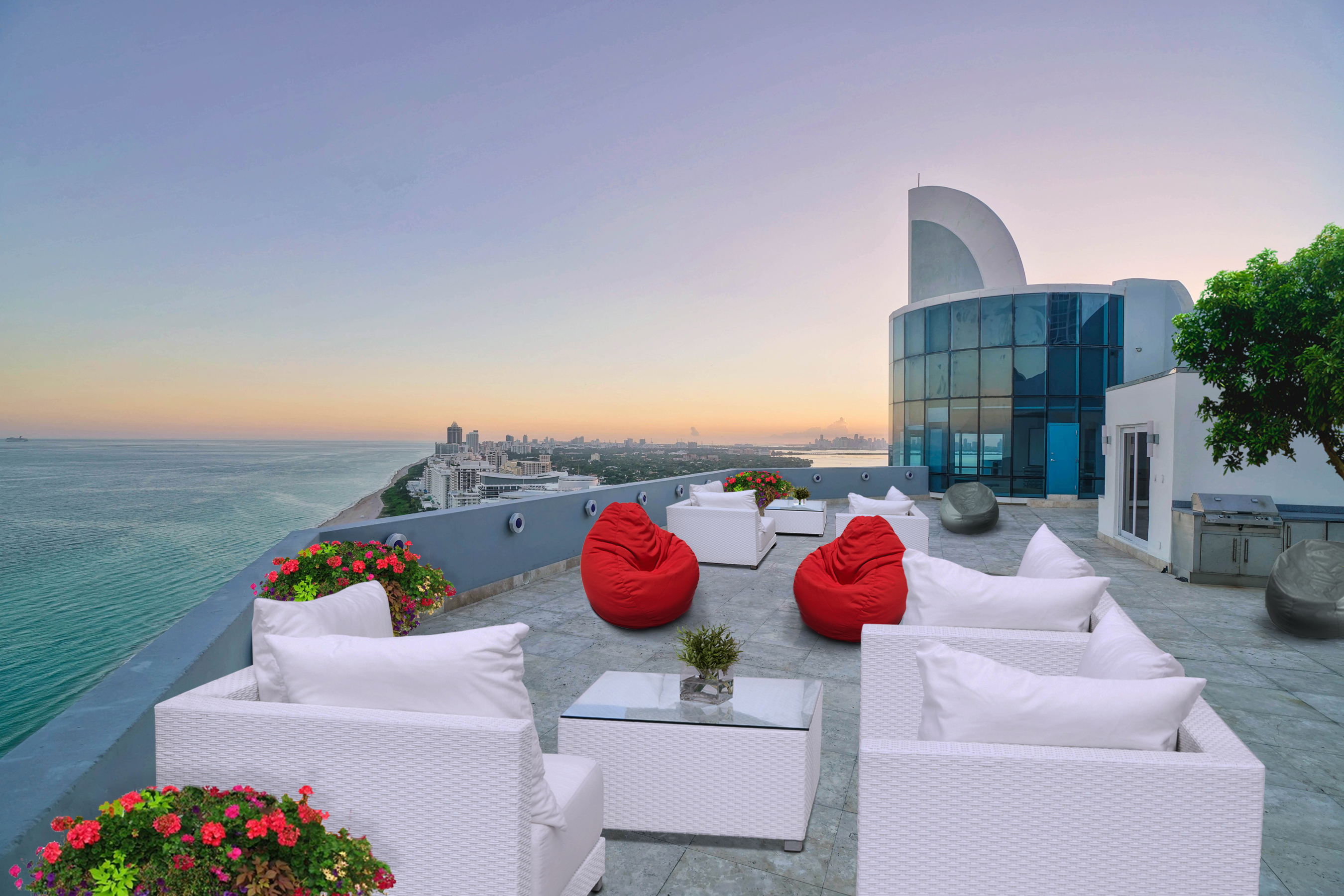 View of a huge rooftop deck with white furniture with an ocean view of Miami Beach in the back left.