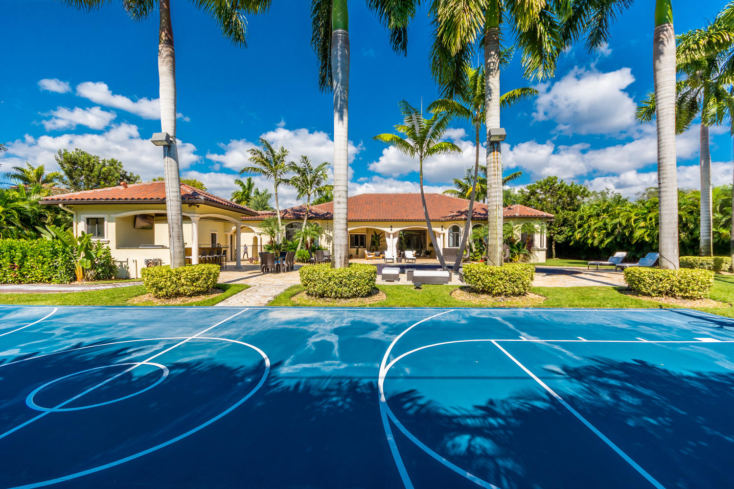 A blue basketball court outside a mediterranean home in Pinecrest, with an orange roof.