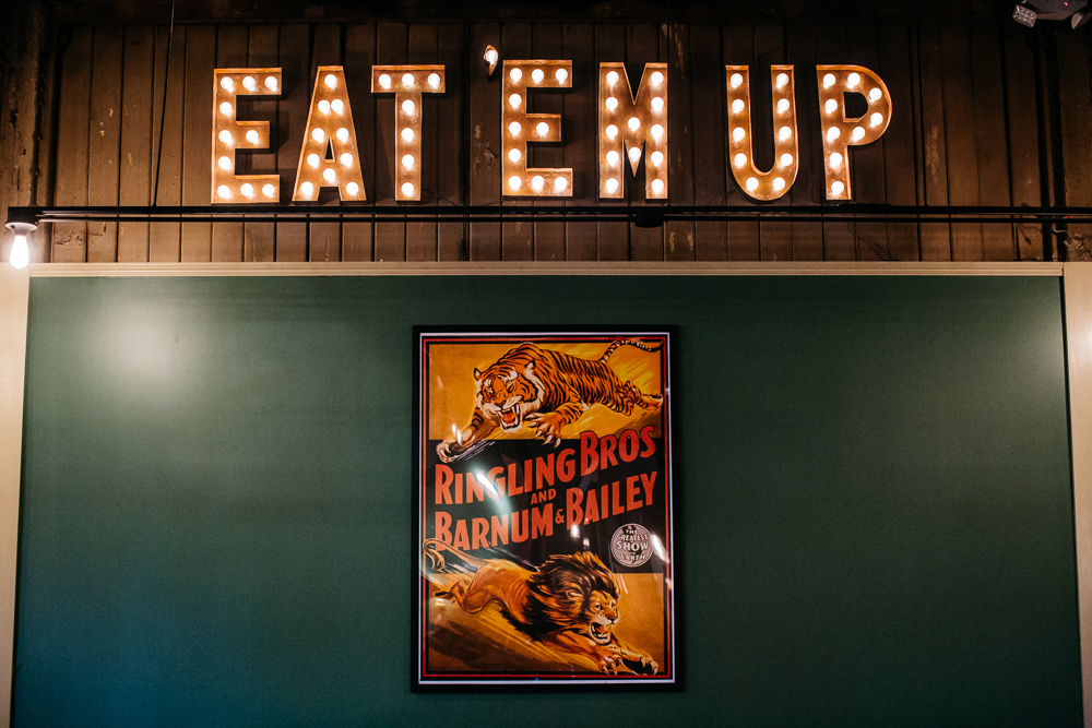 A neon sign on the wooden green wall says Eat ‘Em Up. There’s a poster from the Ringling Bros. &amp; Barnum and Bailey circus, too