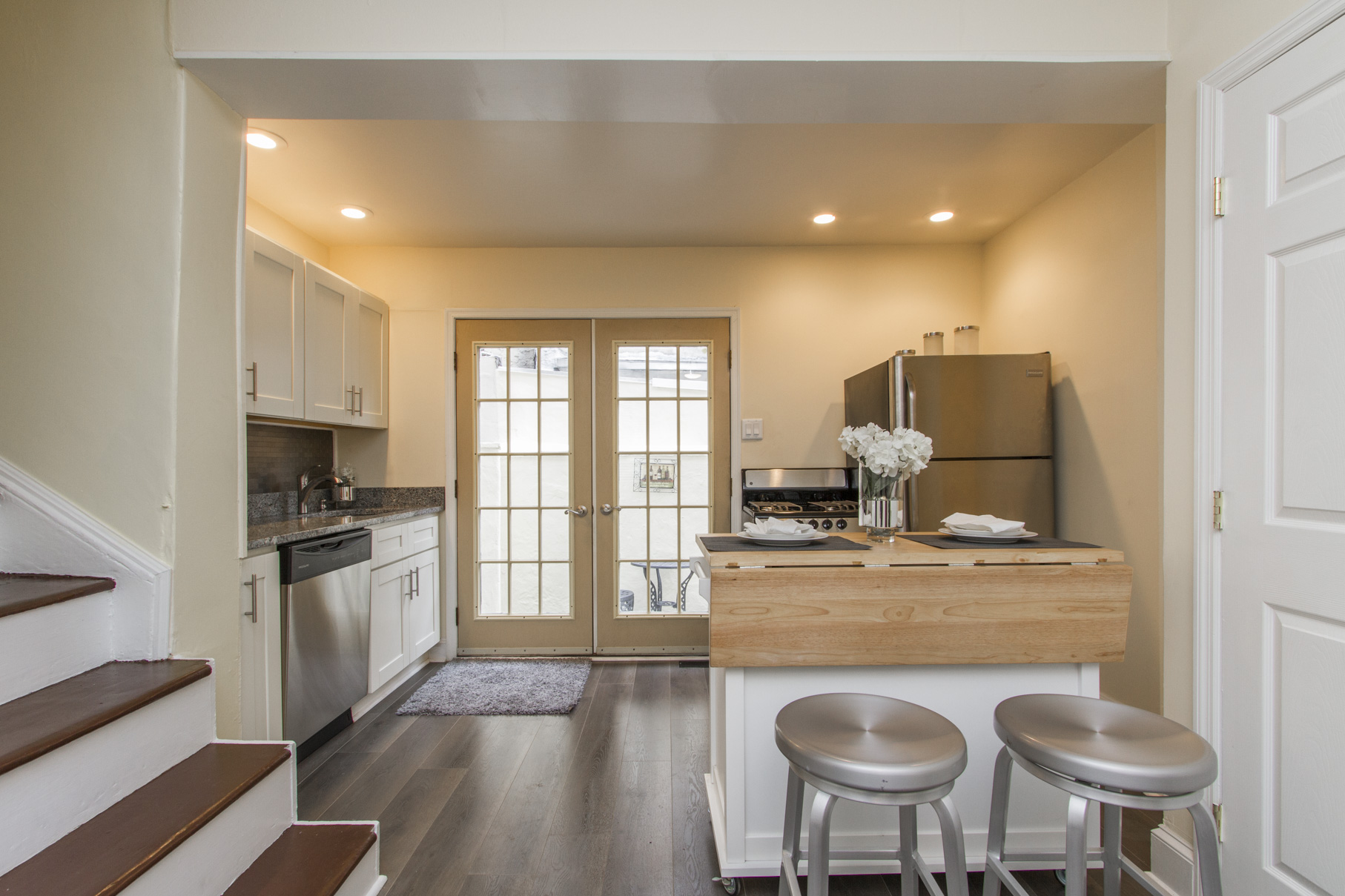 A kitchen with steel bar stools, laminate floors, and French doors.