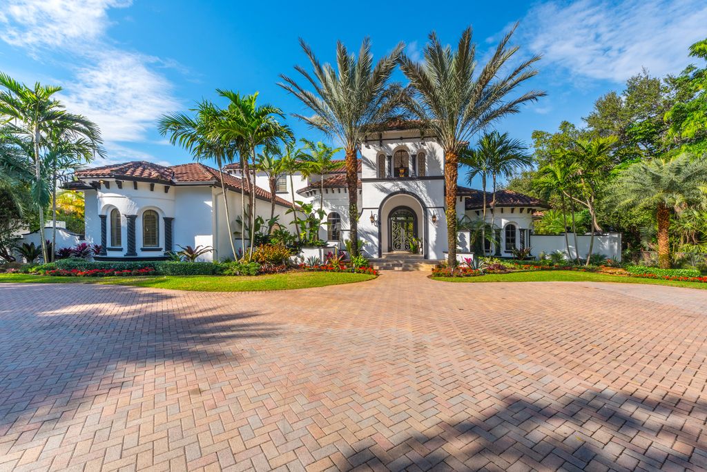 A gorgeous white Mediterranean home in Pinecrest with glorious palms out front and arched entry.