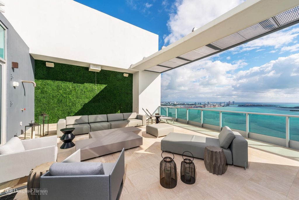 A rooftop deck at a penthouse in Brickell, showing Biscayne Bay views, a turf wall, and contemporary decor.