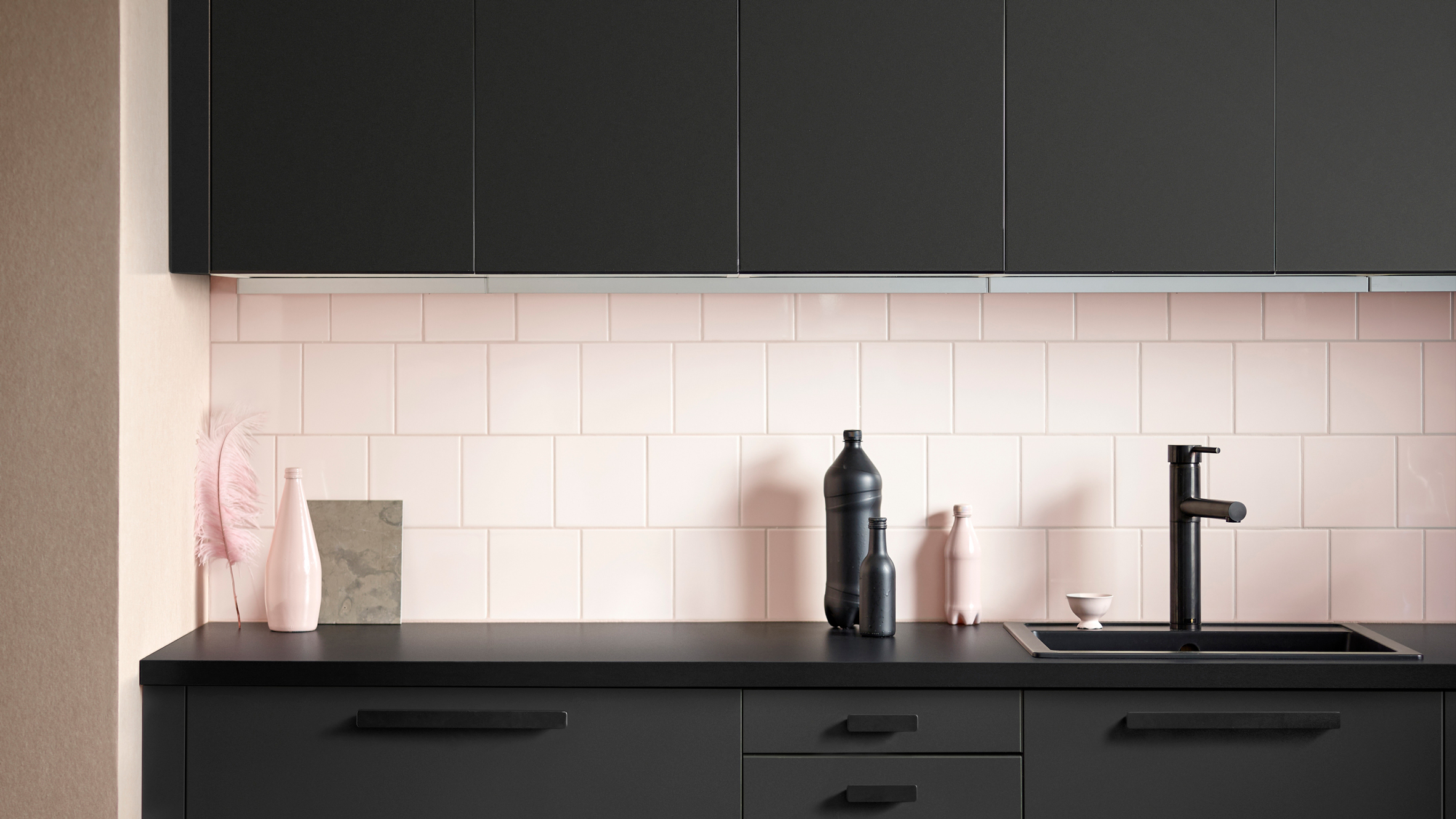 Close up shot of black kitchen counter and cabinets with pale pink tiled backsplash.