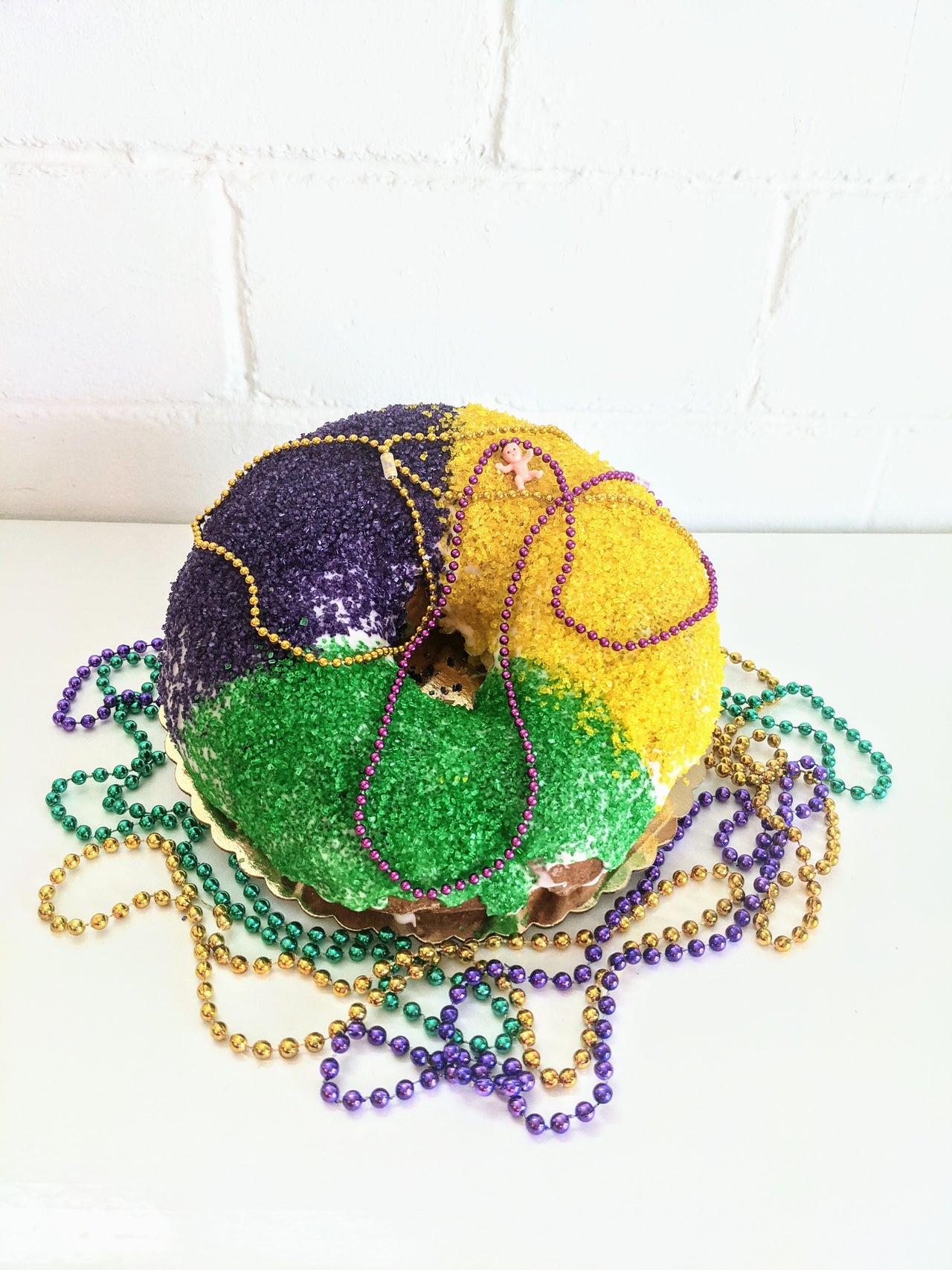 A purple, green, and yellow round cake, with similar colored beaded necklaces on it.