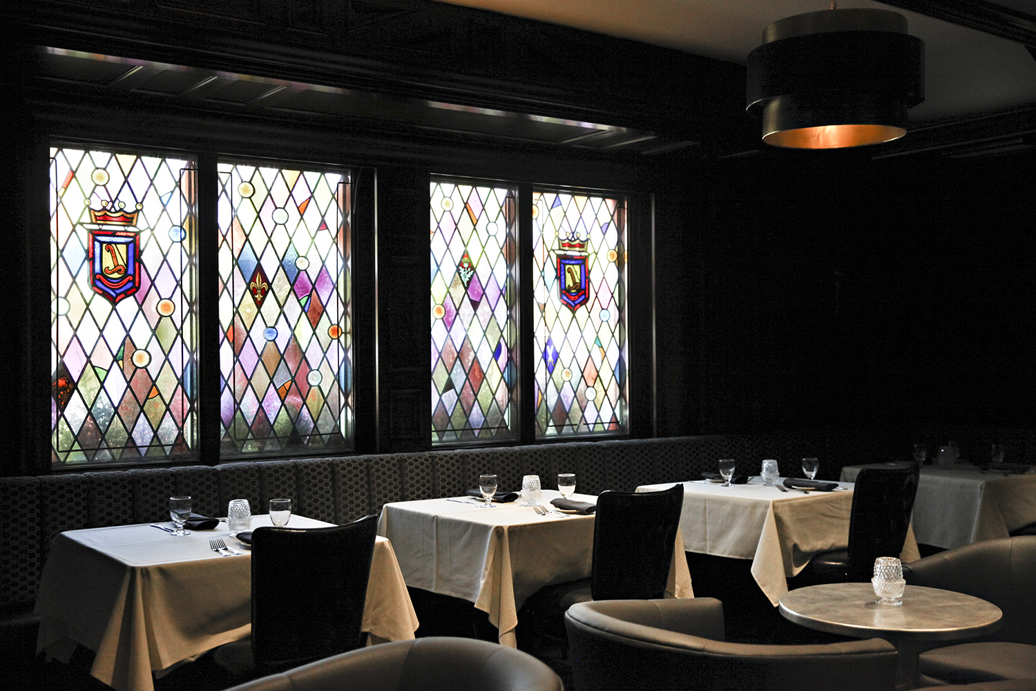 Stained glass windows behind a dining room, set with white tablecloths.